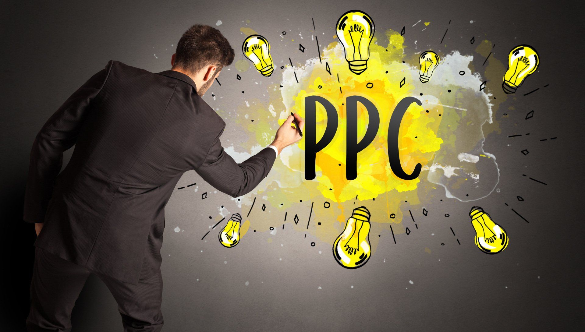 Man in a suit draws on a blackboard with yellow lightbulbs surrounding the letters