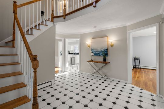 Bright foyer with white staircase, black-and-white tiled floor, and small table under ocean wall art