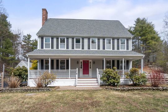 Two-story gray house with white porch, red front door, and a brick chimney in a yard.
