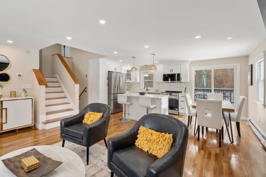 Bright open-concept living and dining room with staircase, black chairs, and kitchen island