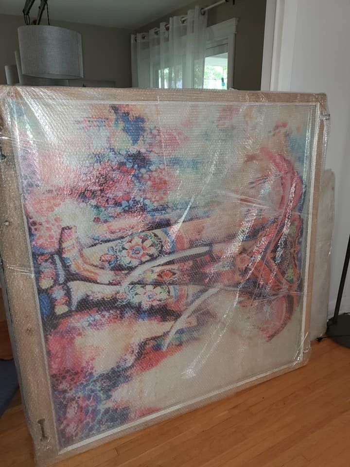 Un grand tableau est emballé dans du plastique et posé sur un plancher en bois.