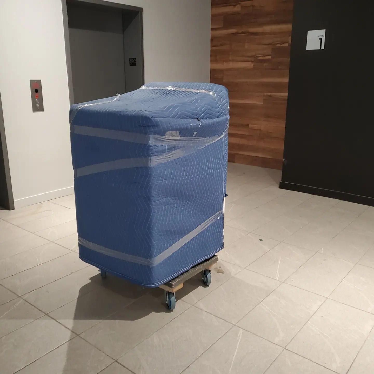 Une boîte bleue enveloppée de plastique est posée sur un chariot dans une pièce.