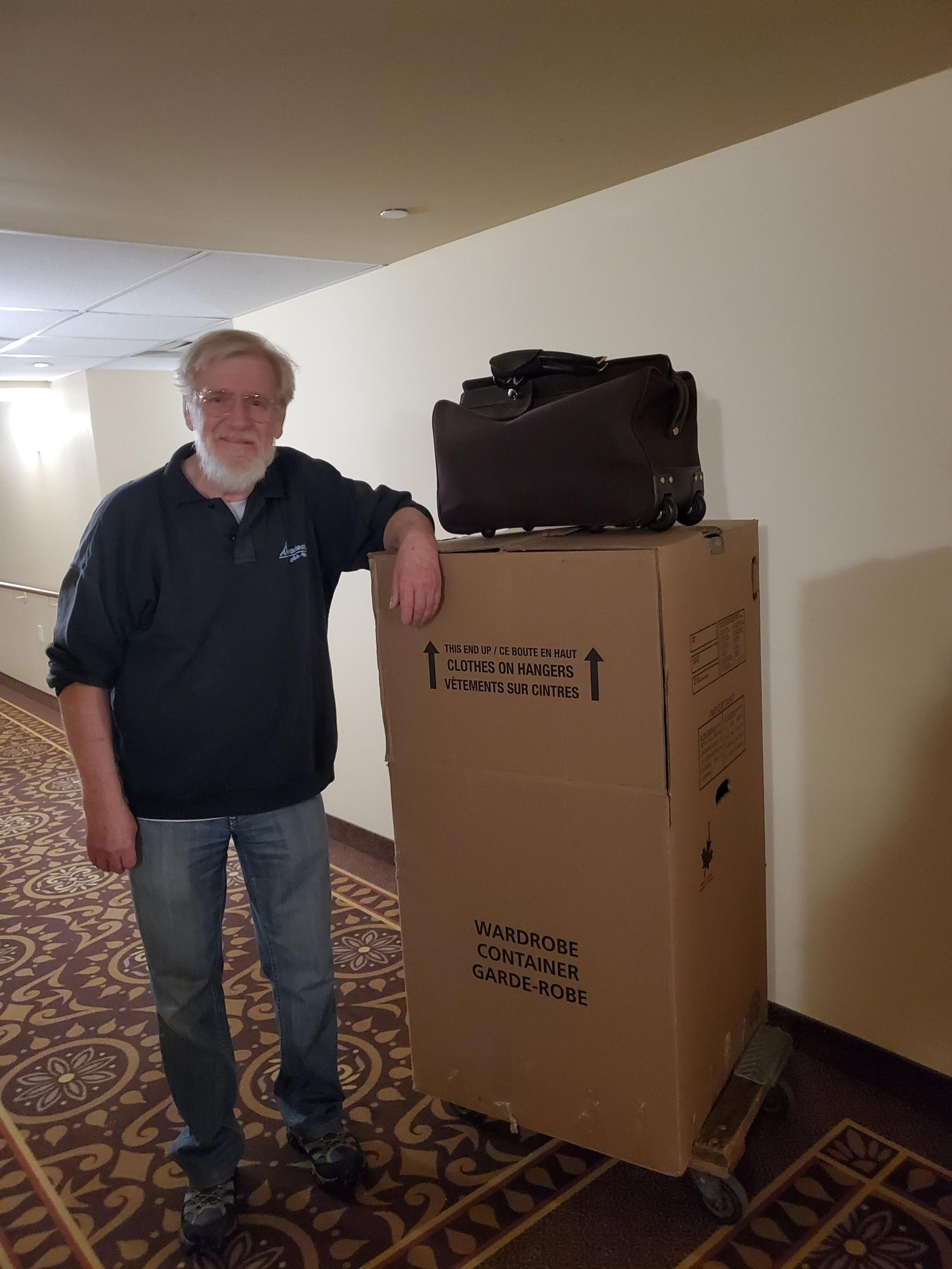 Un homme se tient à côté d'une grande boîte en carton avec une valise dessus.
