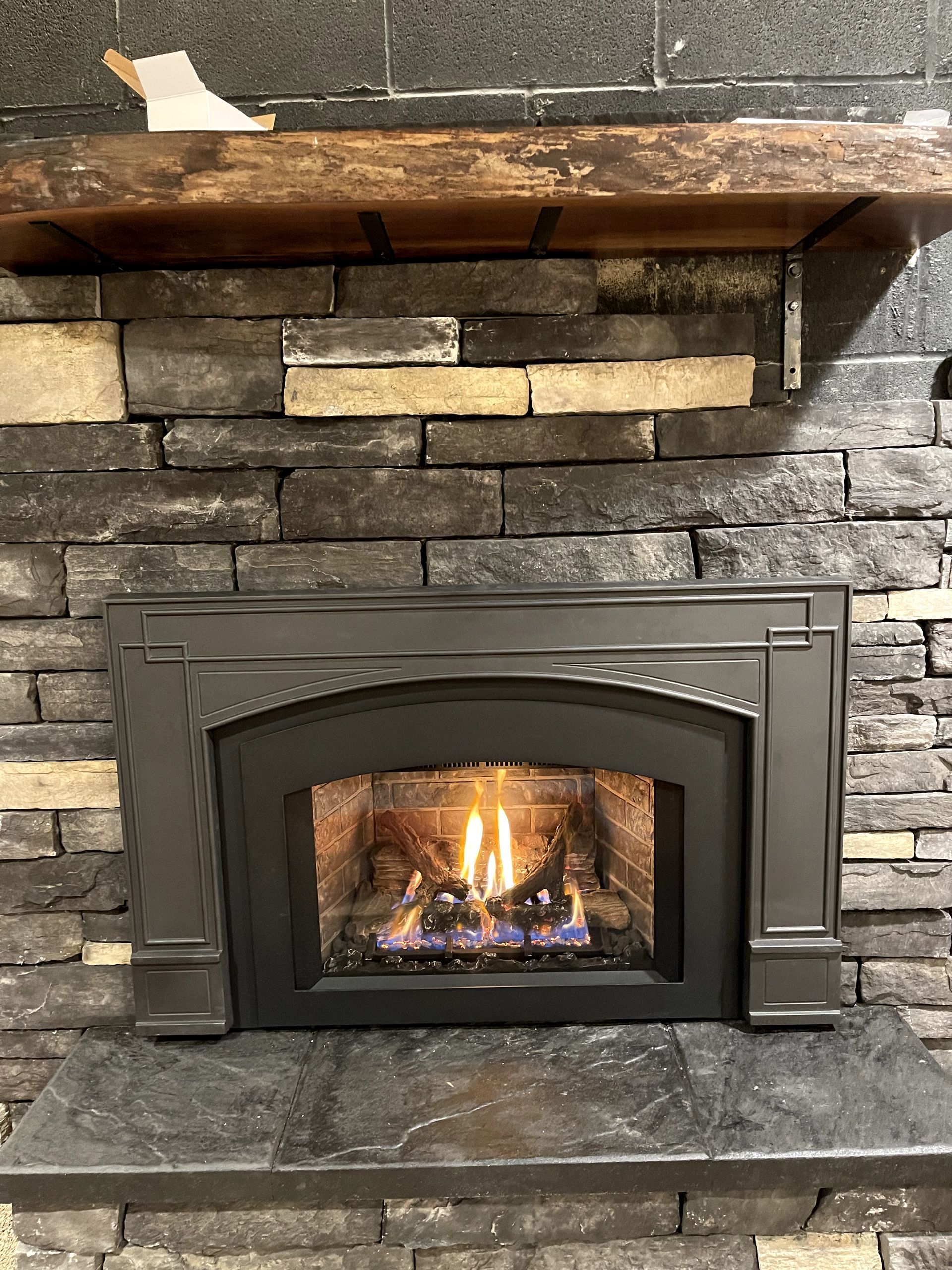 A fireplace with a brick wall and a wooden mantle.