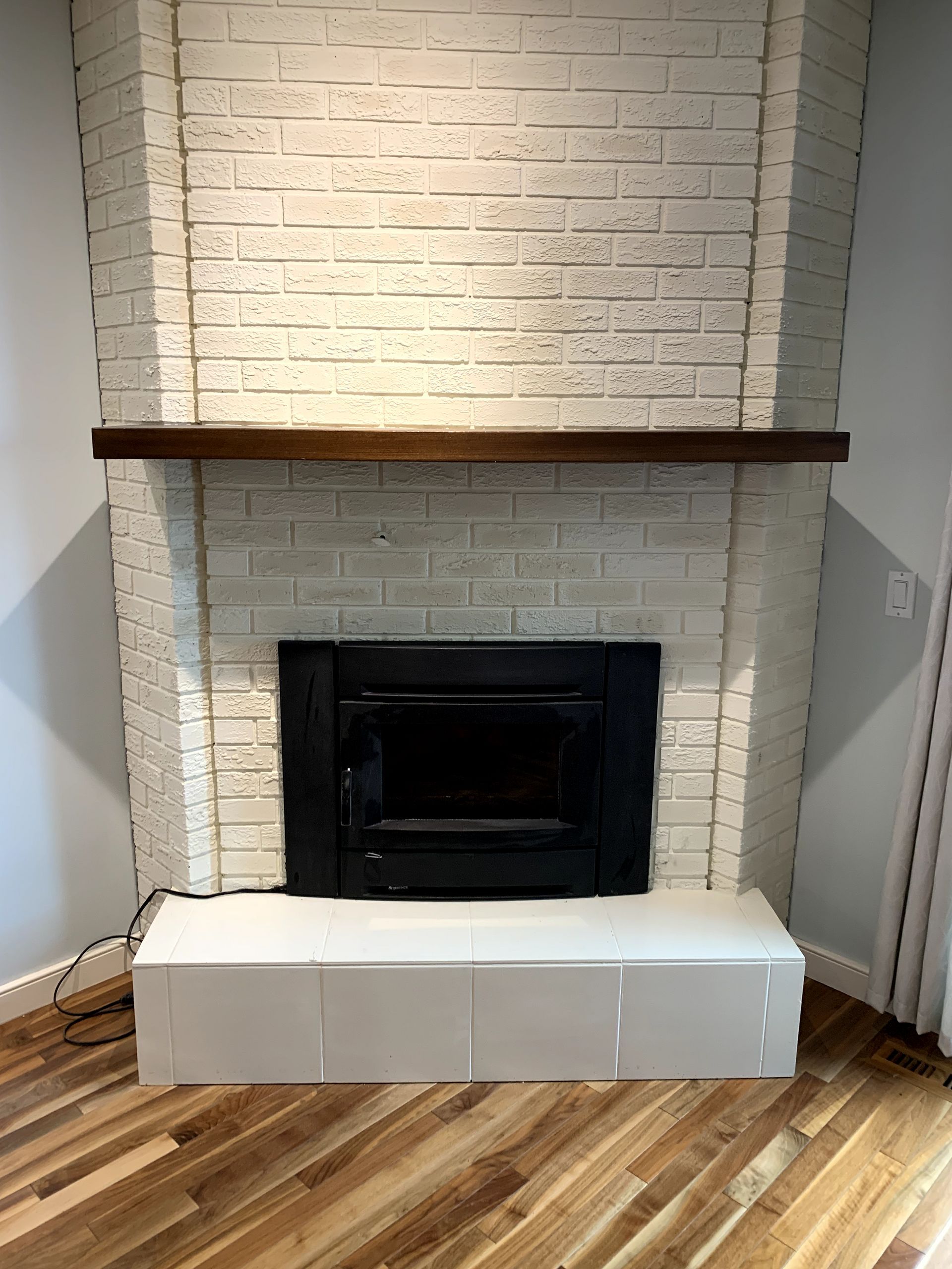 A white brick fireplace with a wooden mantle in a living room.