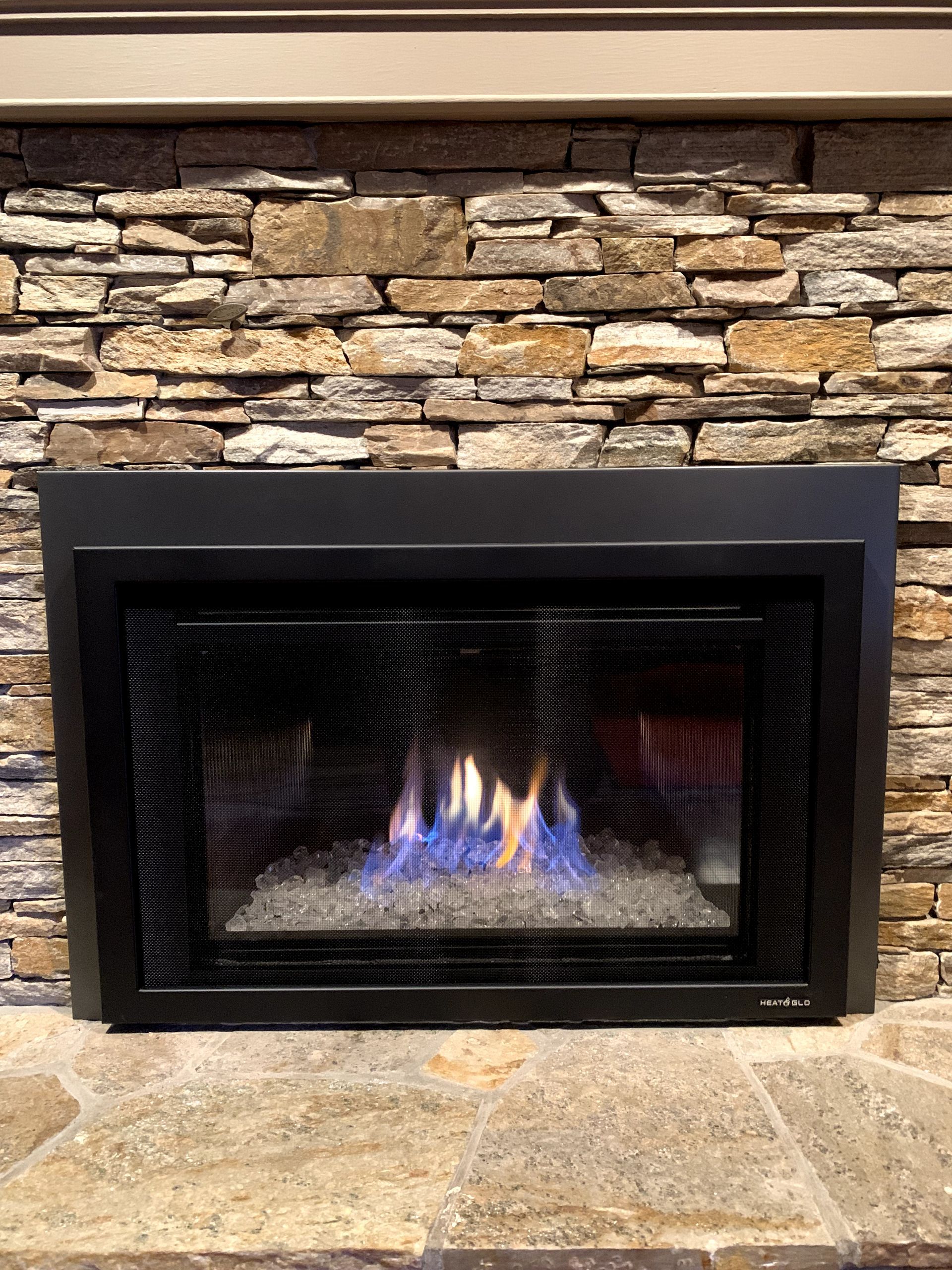 A fireplace with a stone wall behind it and blue flames coming out of it.