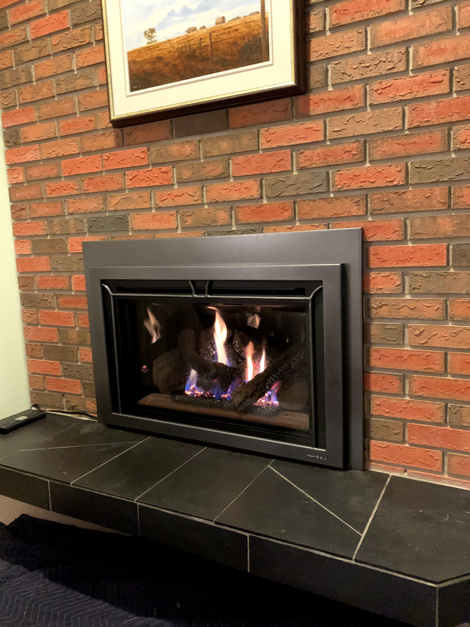 A fireplace with a brick wall and a picture on the wall above it.