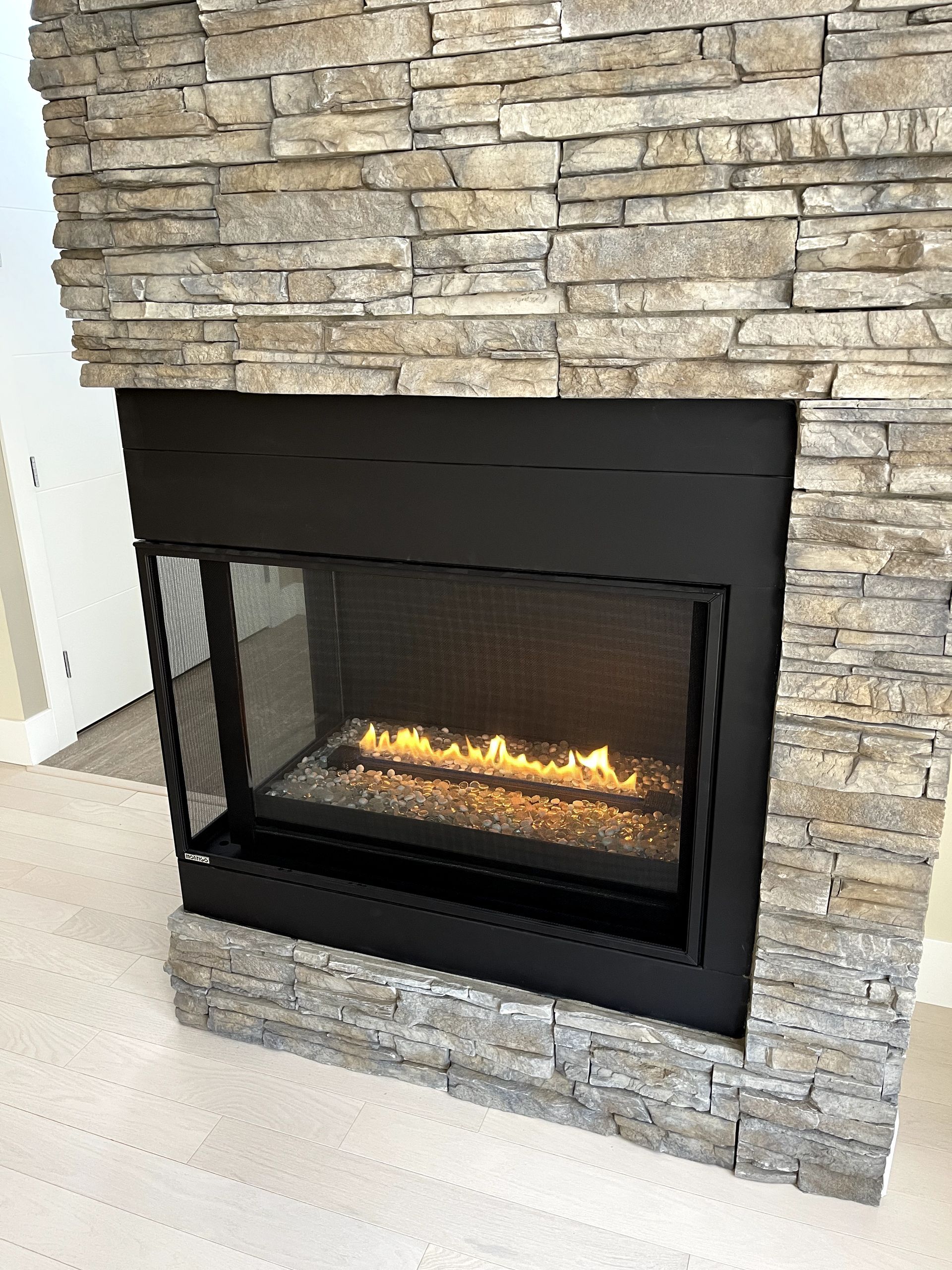 A fireplace with a stone wall and a glass door in a living room.