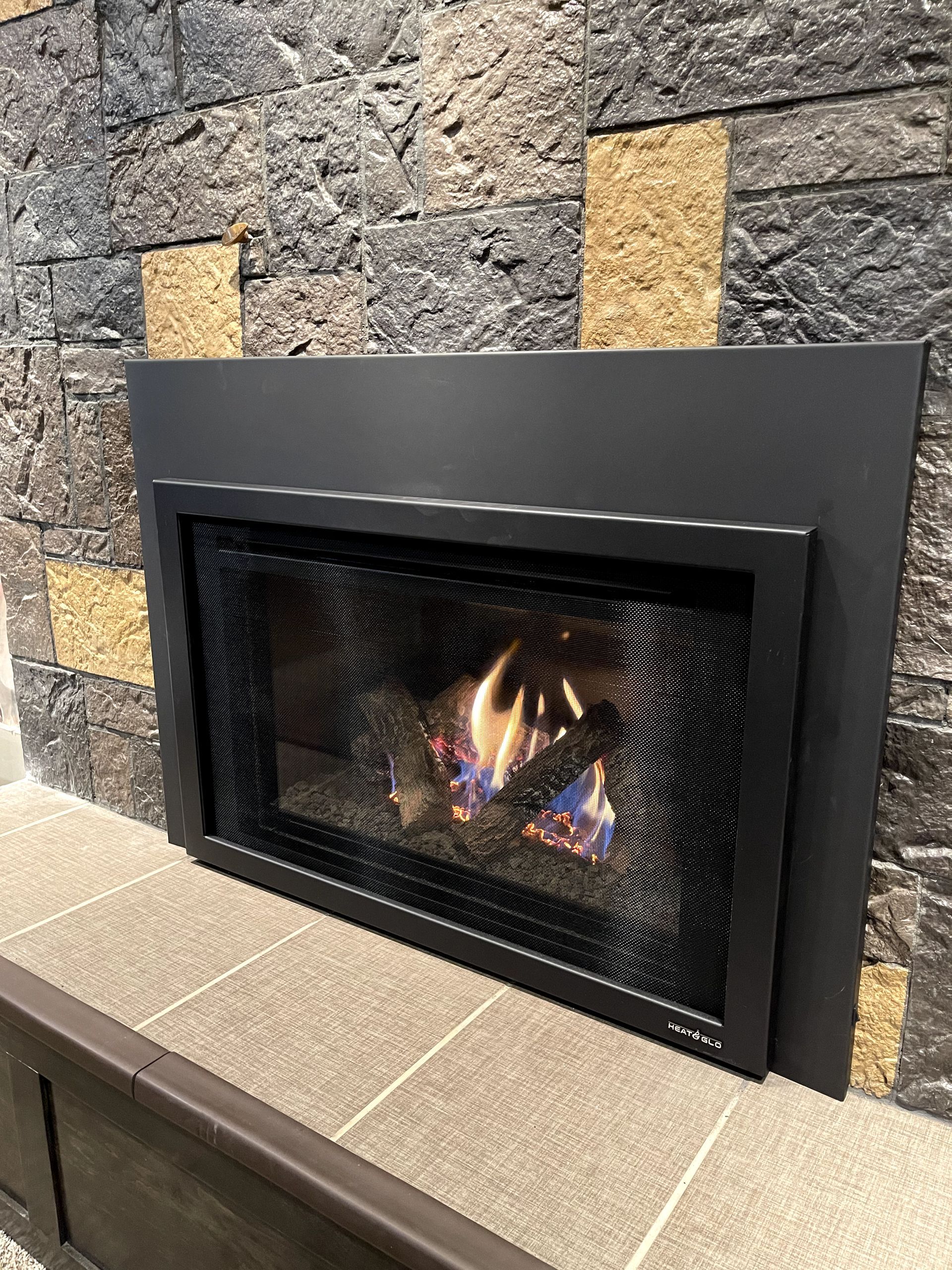A fireplace with a mesh screen is built into a stone wall.