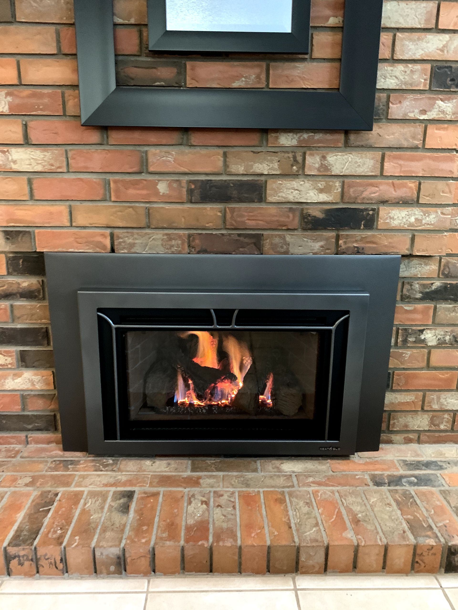 A fireplace with a black frame and a brick wall.