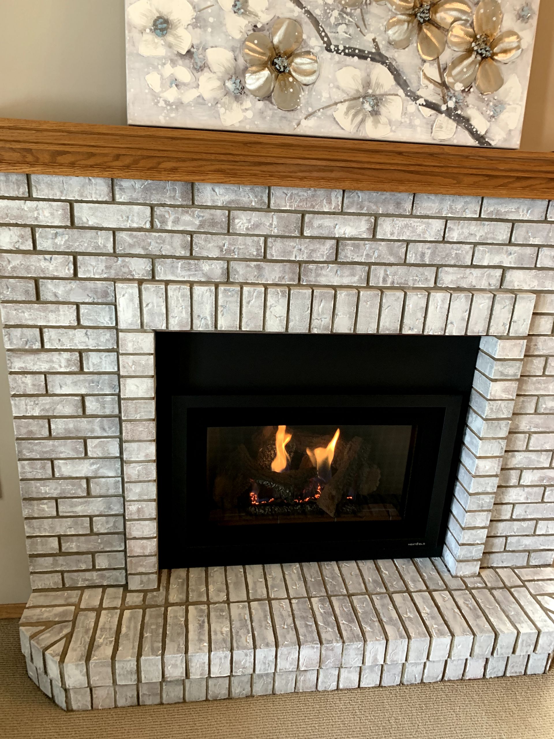 A fireplace with a painting of flowers on the mantle.