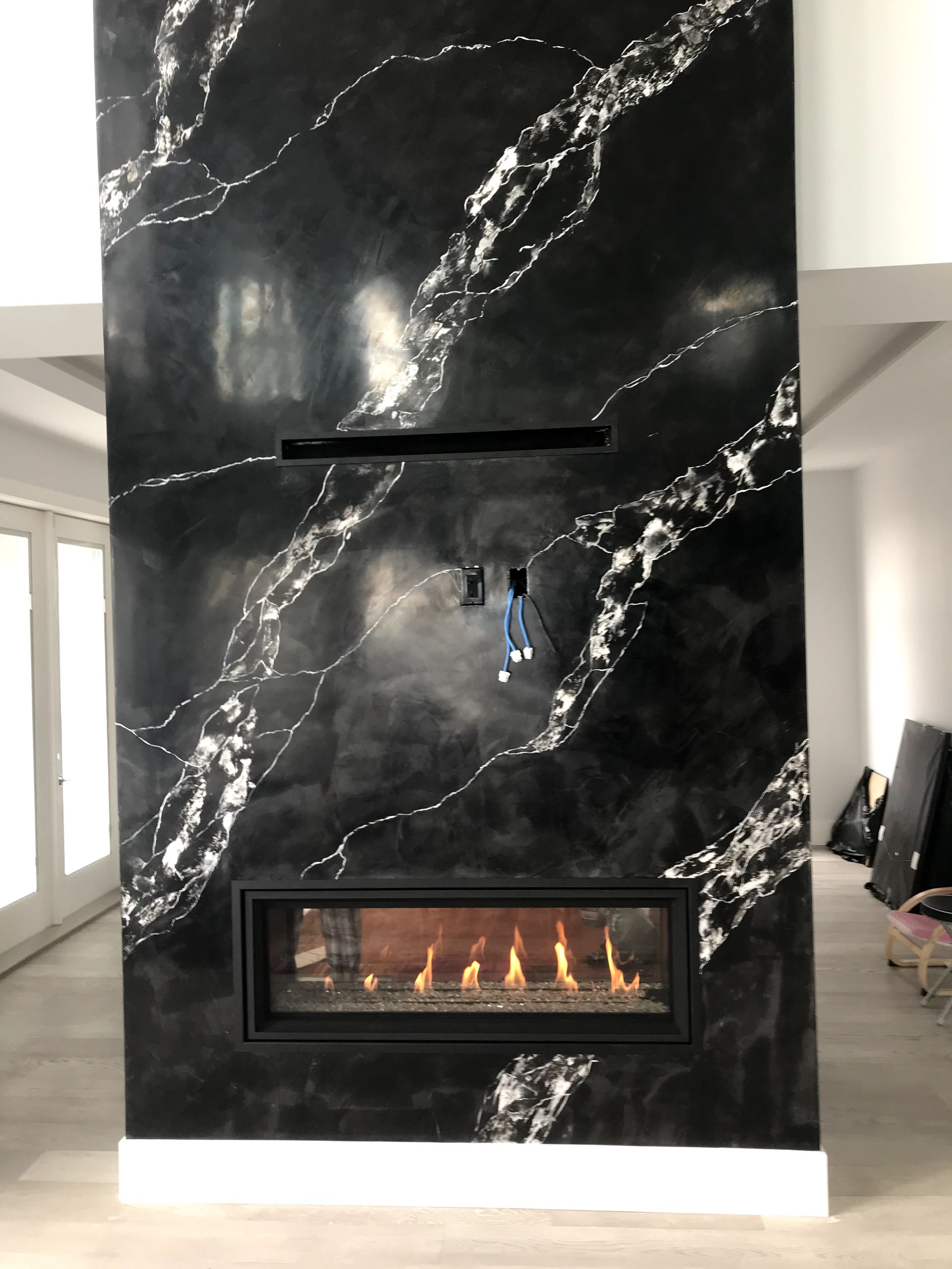 A fireplace in a living room with a black and white marble wall.