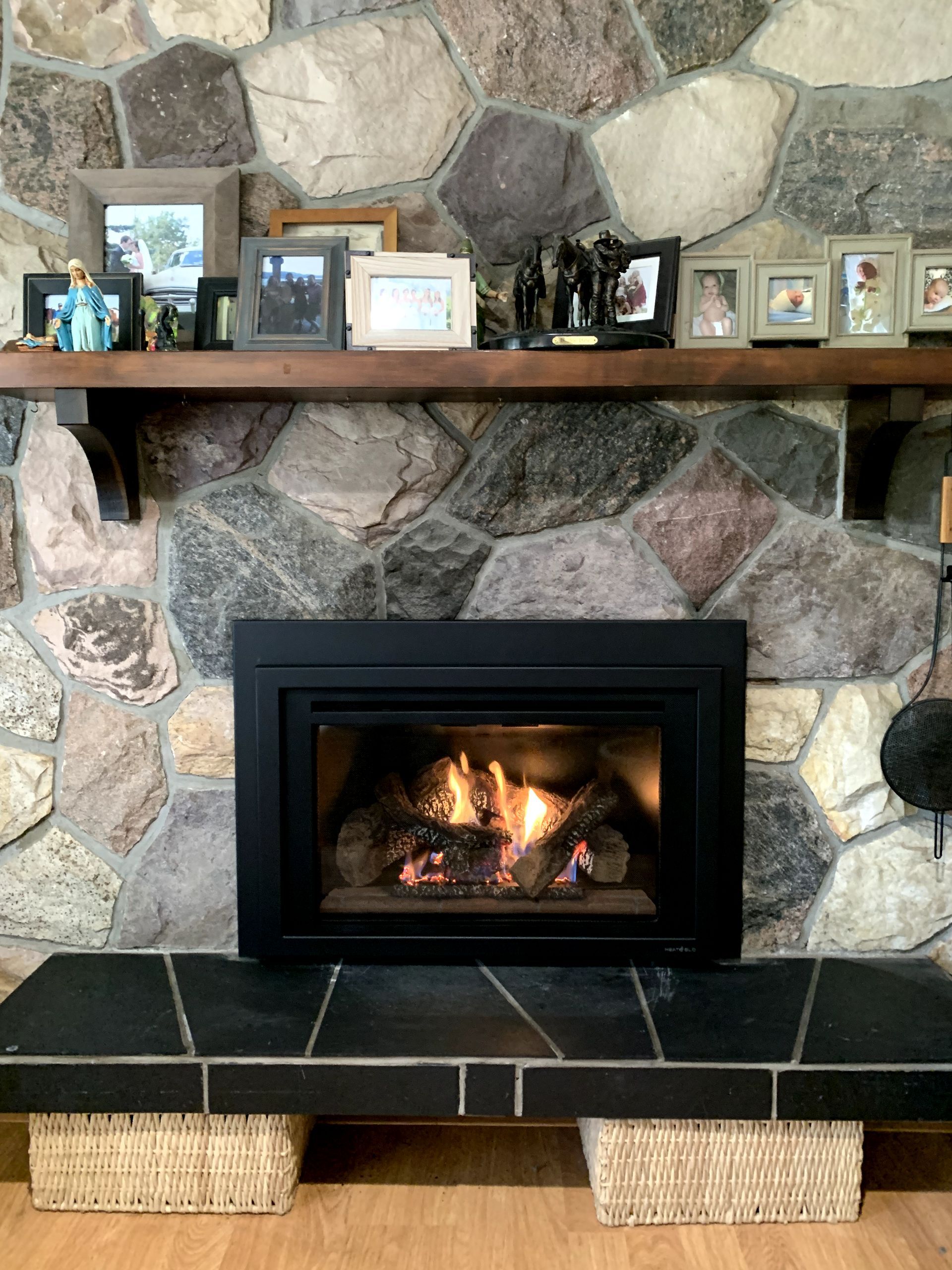 A fireplace in a living room with a stone wall and a wooden mantle.