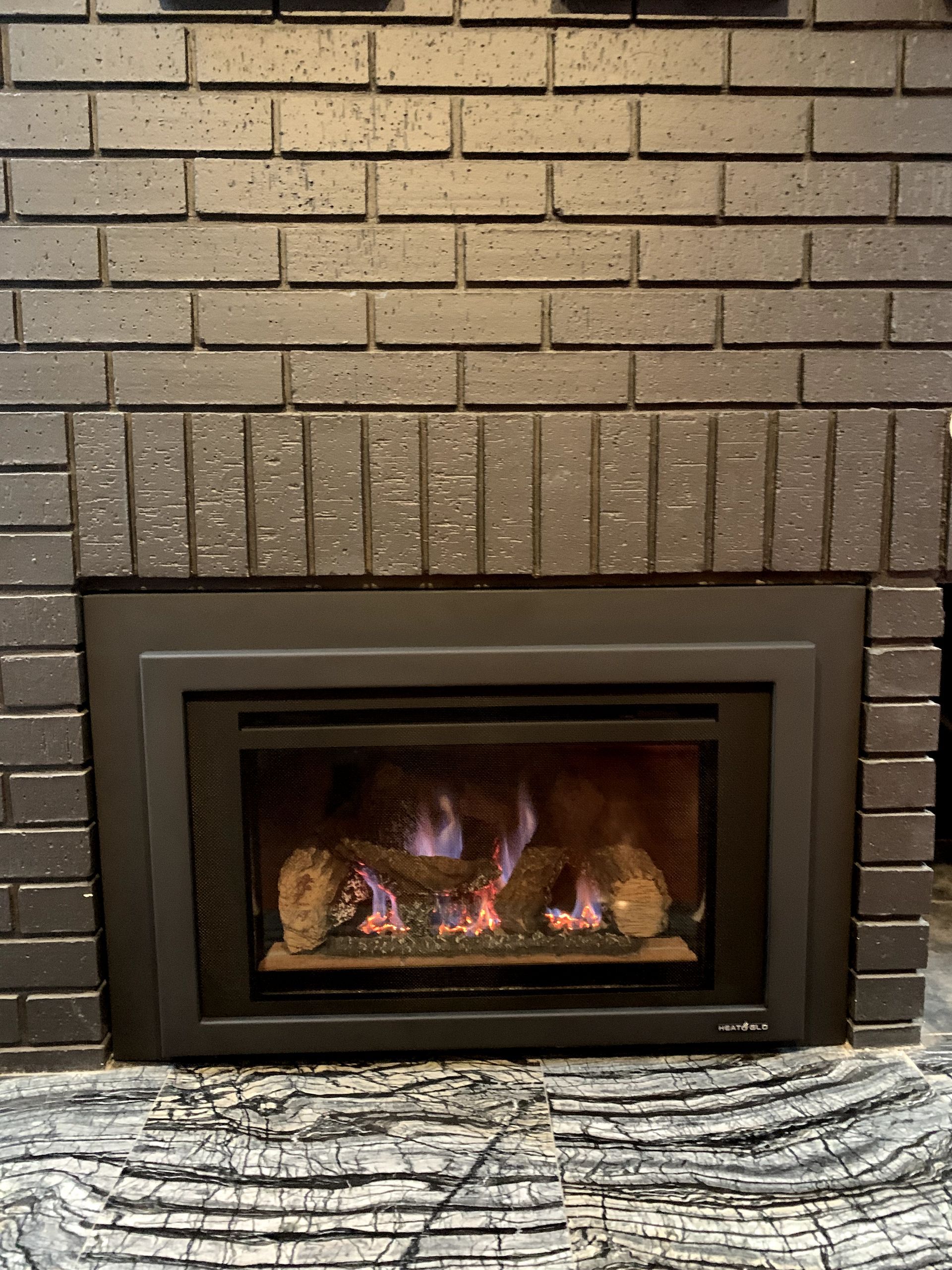 A brick fireplace with a gas fireplace insert in it.