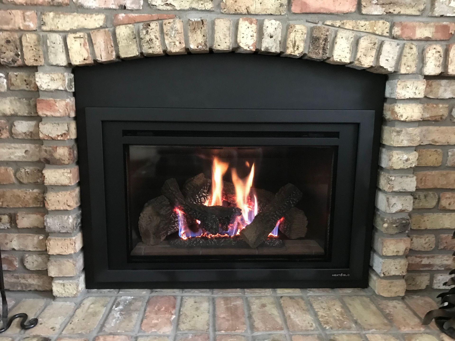 A brick fireplace with a gas fireplace insert in it.