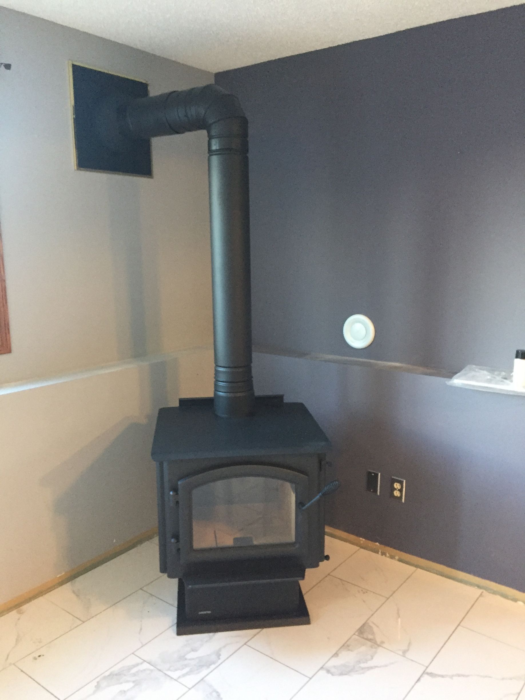 A black wood stove is sitting in a corner of a room.