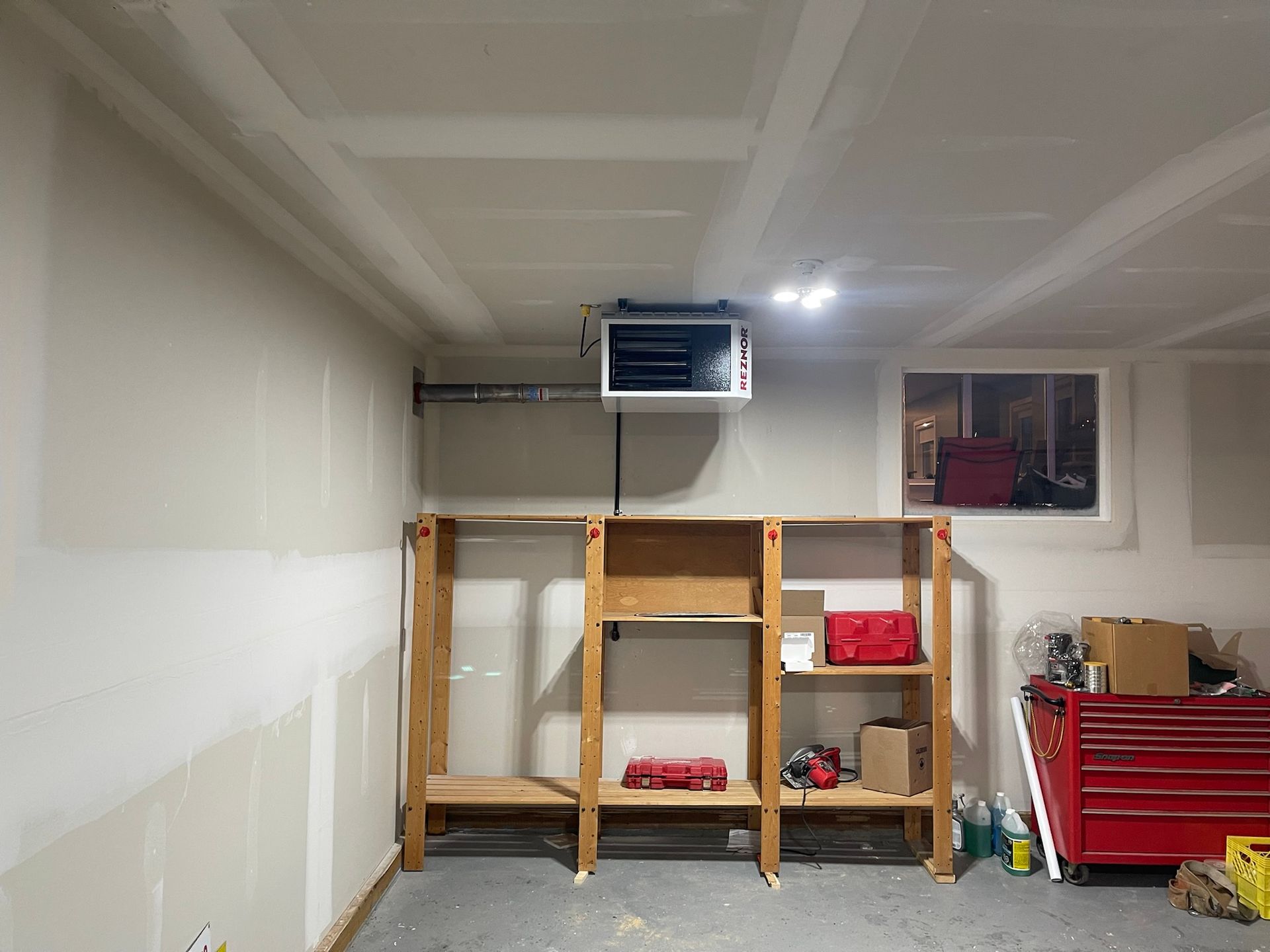 A garage with a heater hanging from the ceiling and shelves.