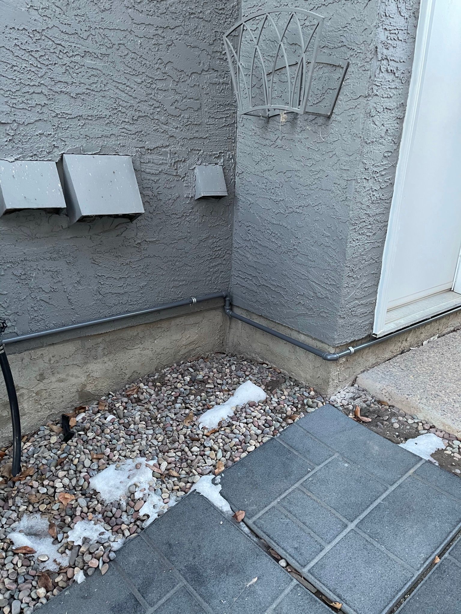 A corner of a building with gravel and snow on the ground.