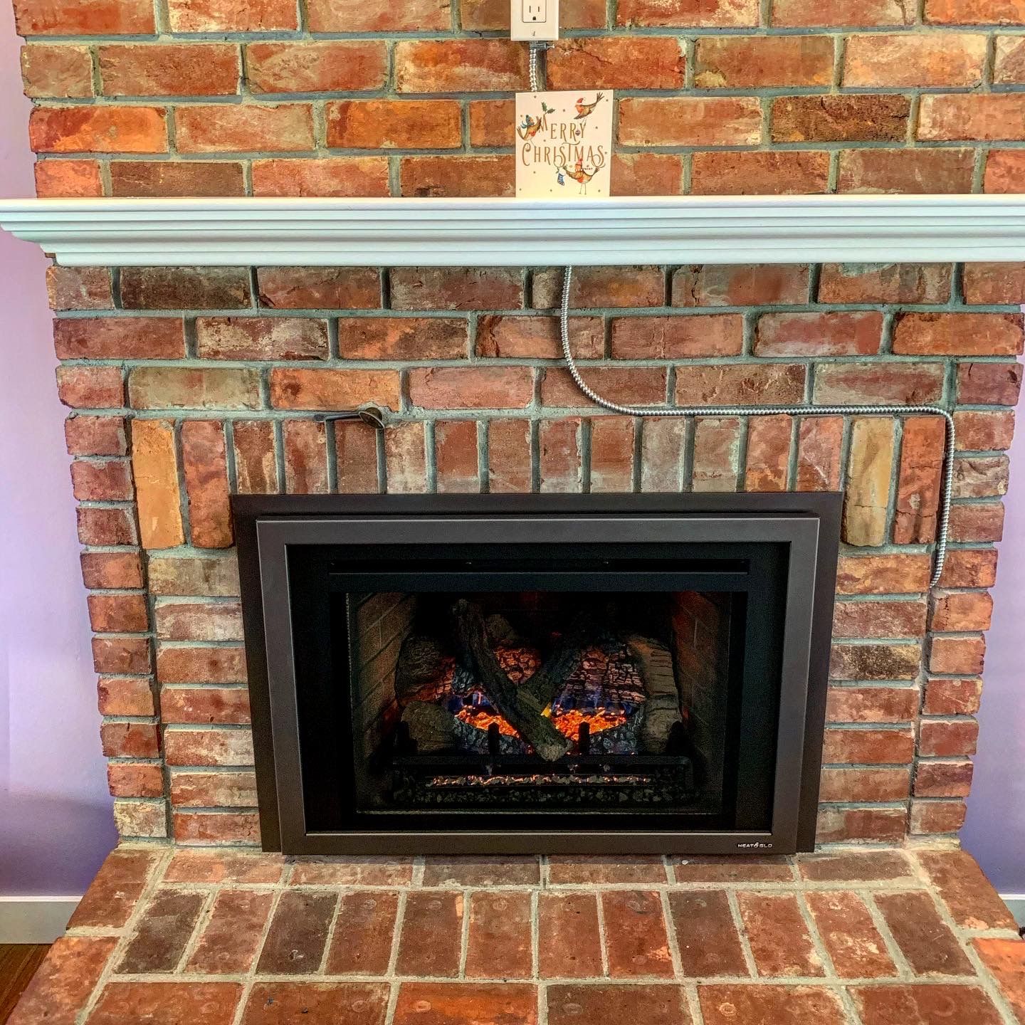 A brick fireplace with a gas fireplace insert in a living room.