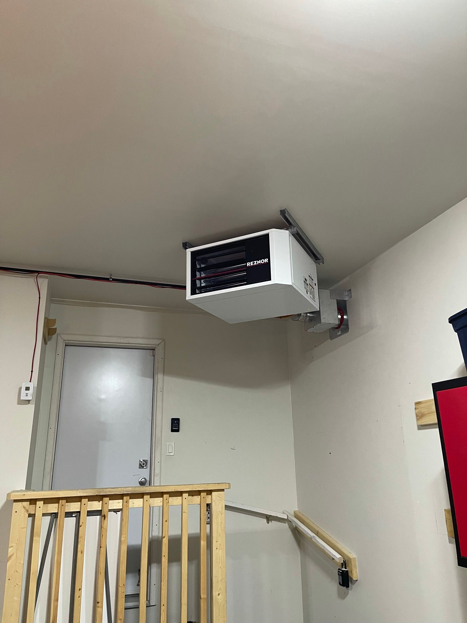 A projector is hanging from the ceiling of a room next to a staircase.