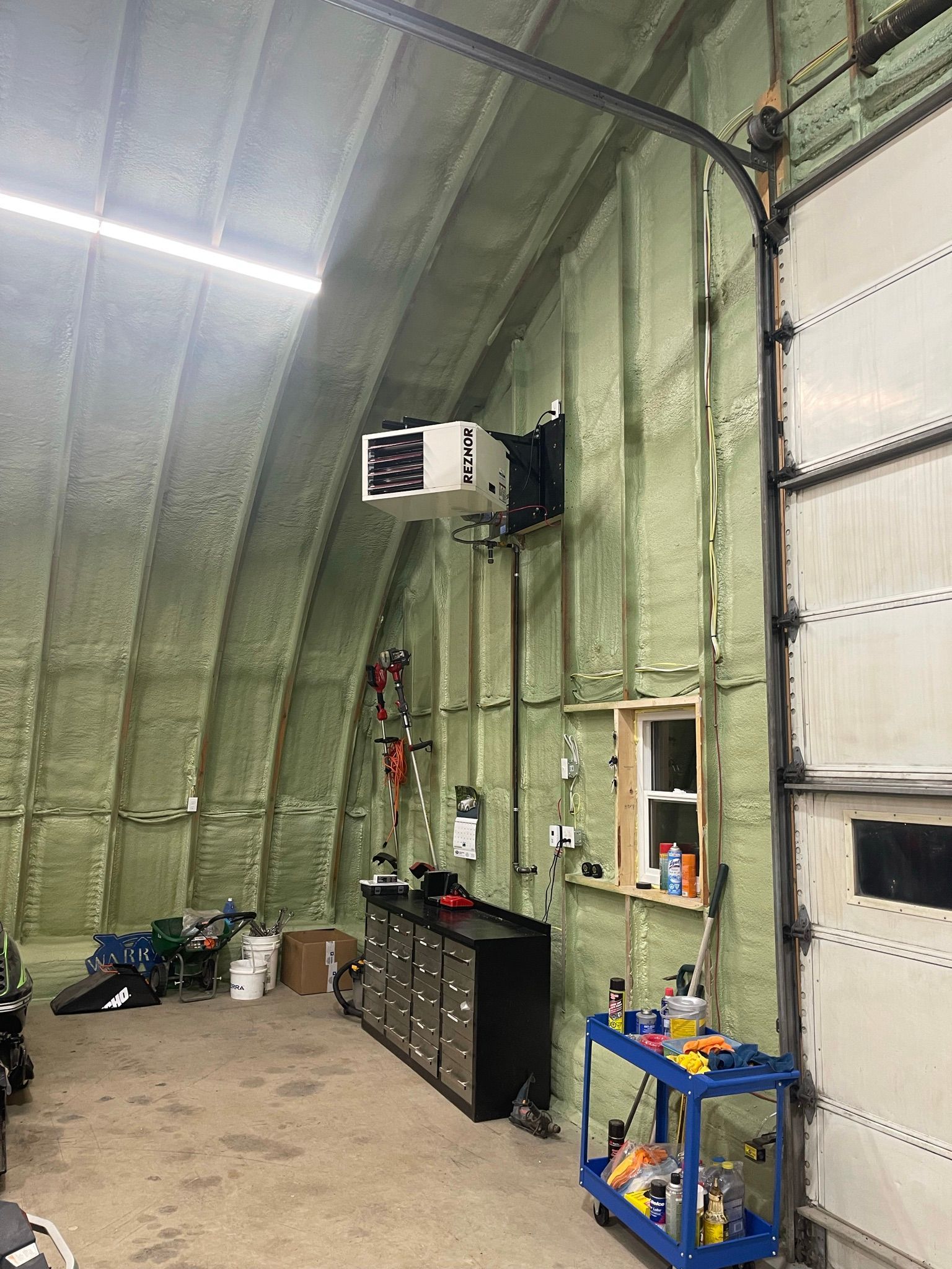 A garage with a heater hanging from the ceiling and a blue cart.