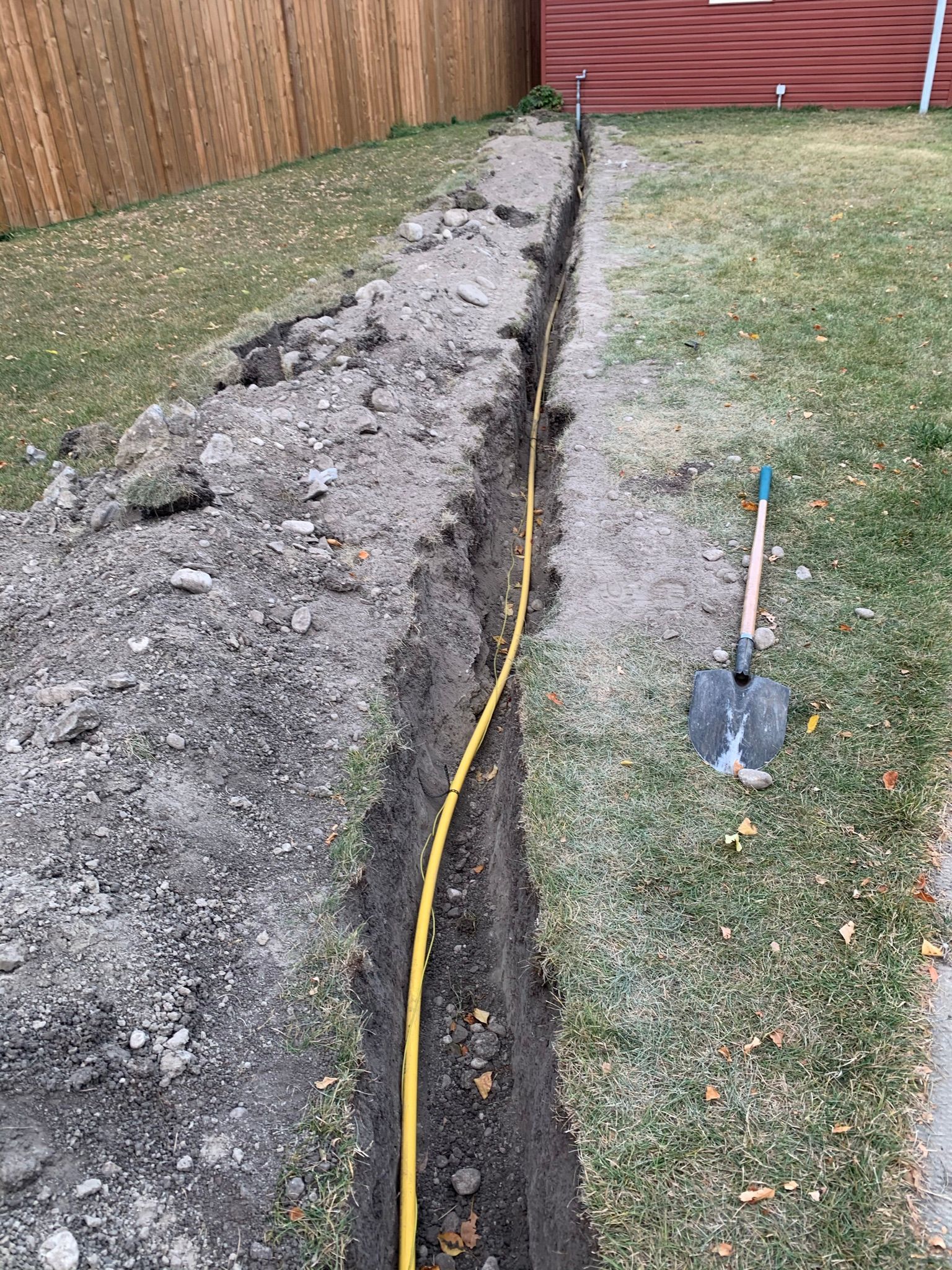 A shovel is sitting in the dirt next to a trench.