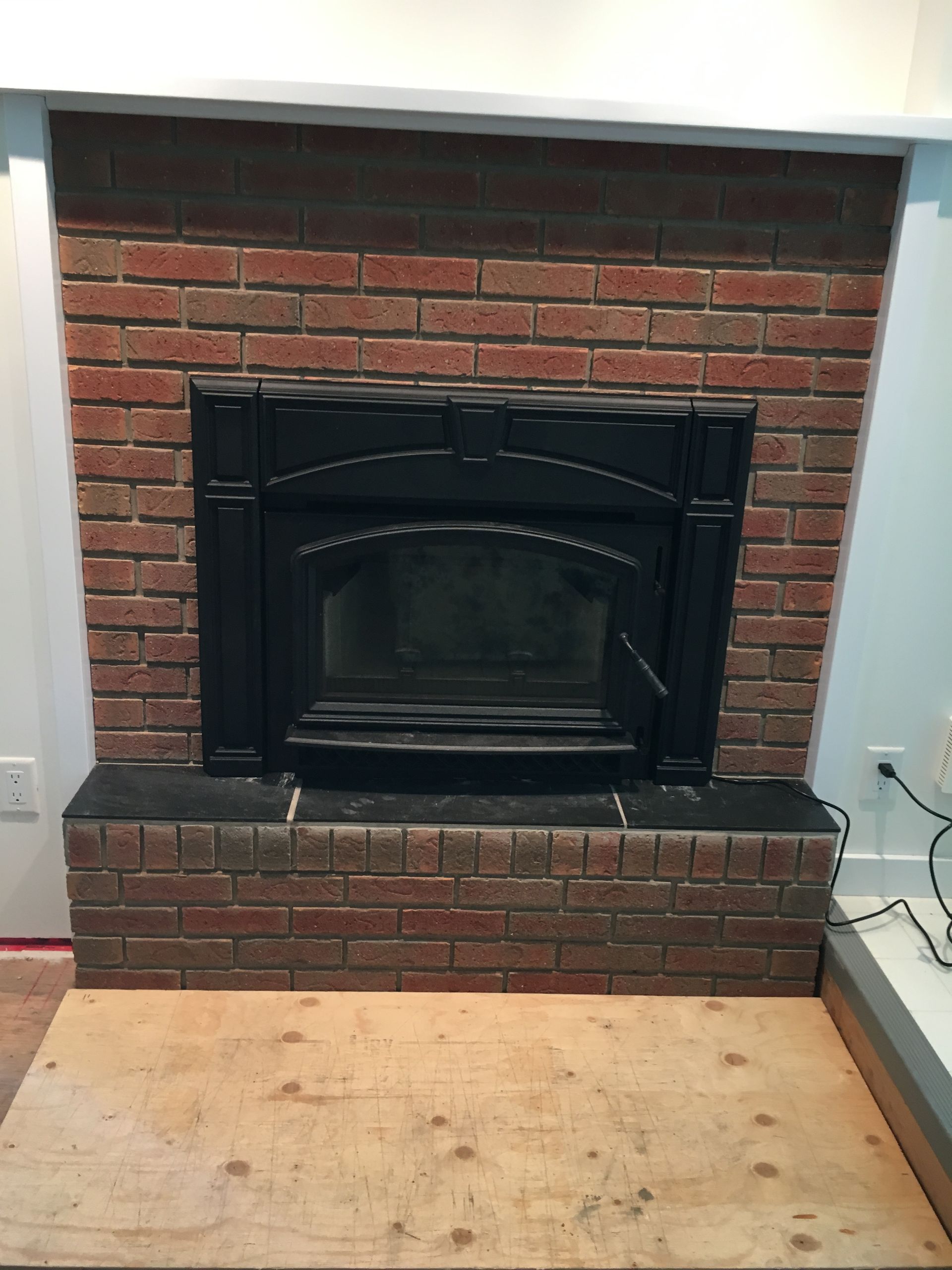 A brick fireplace with a wooden table in front of it.