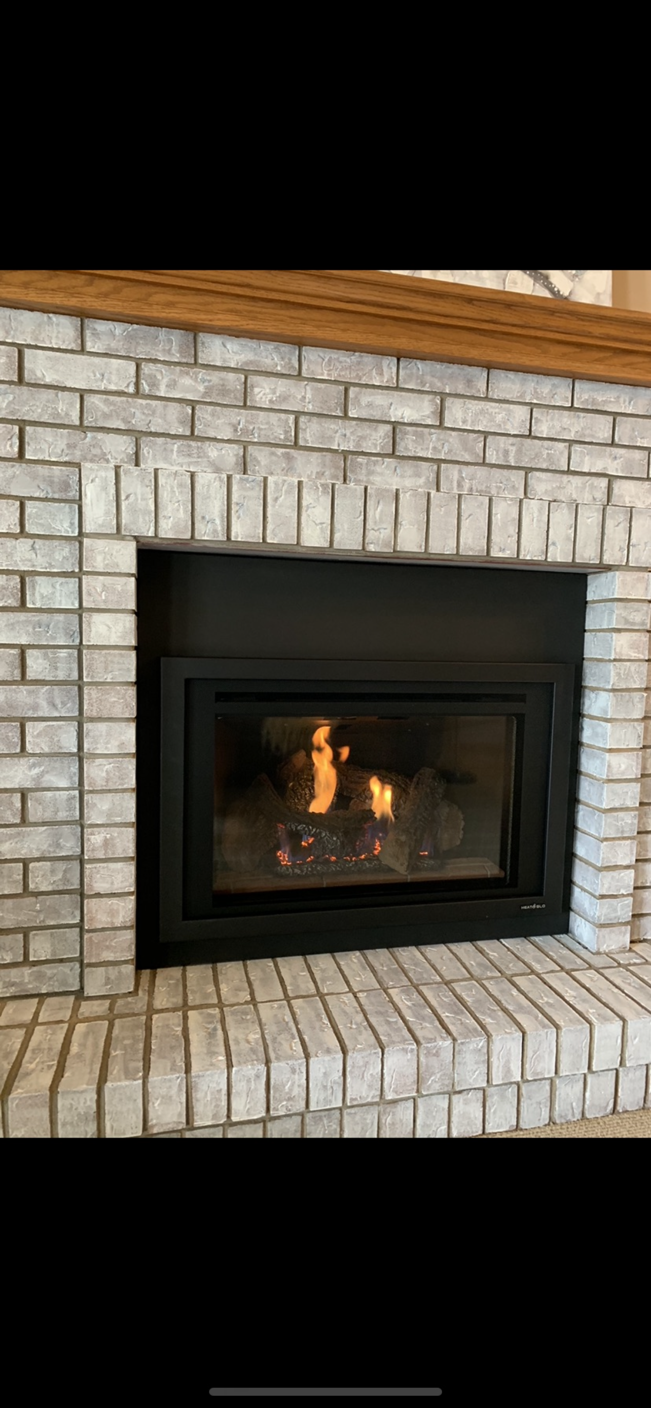 A white brick fireplace with a gas fireplace insert in it.