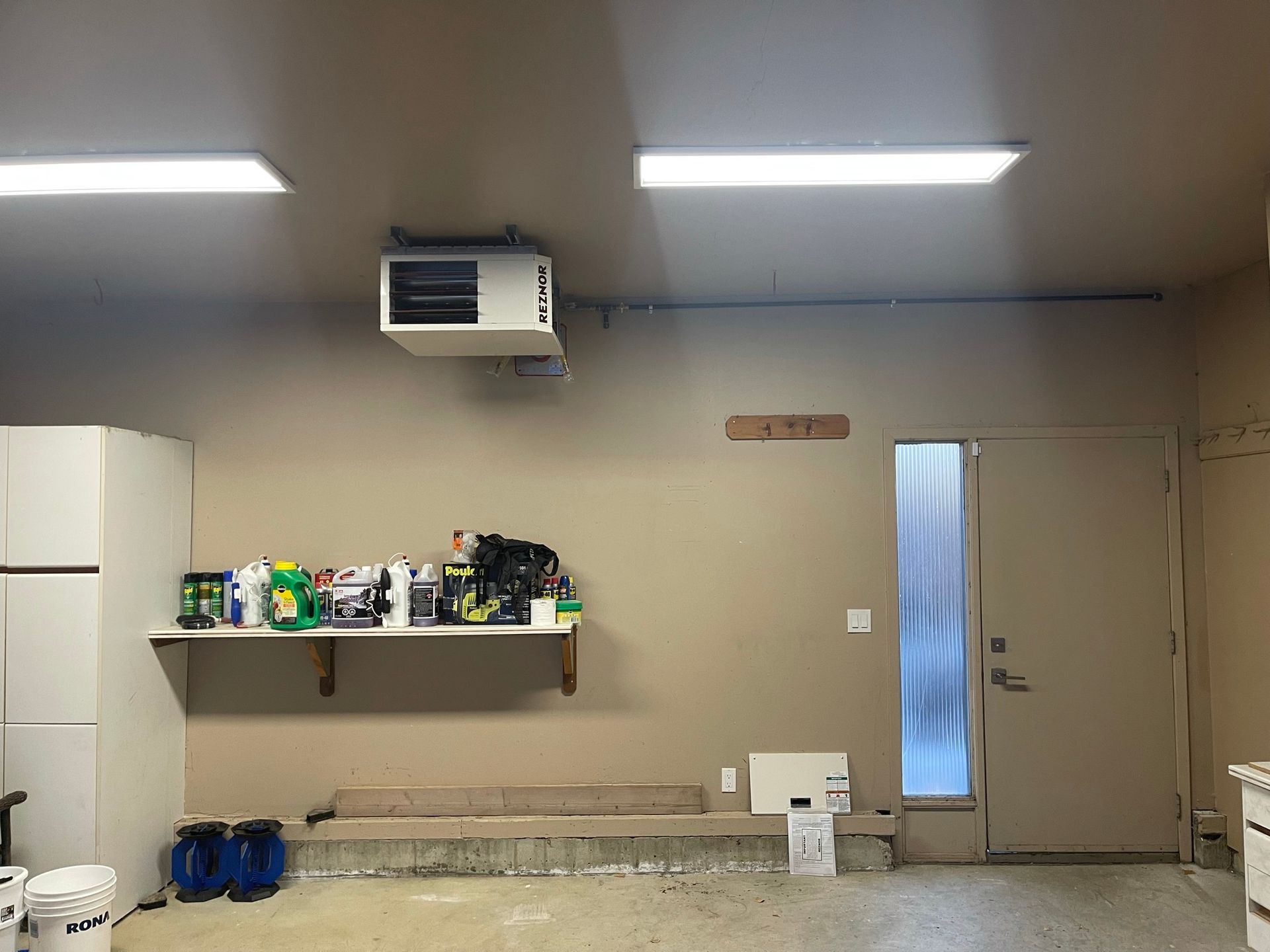 A garage with a refrigerator and a shelf with cleaning supplies on it.