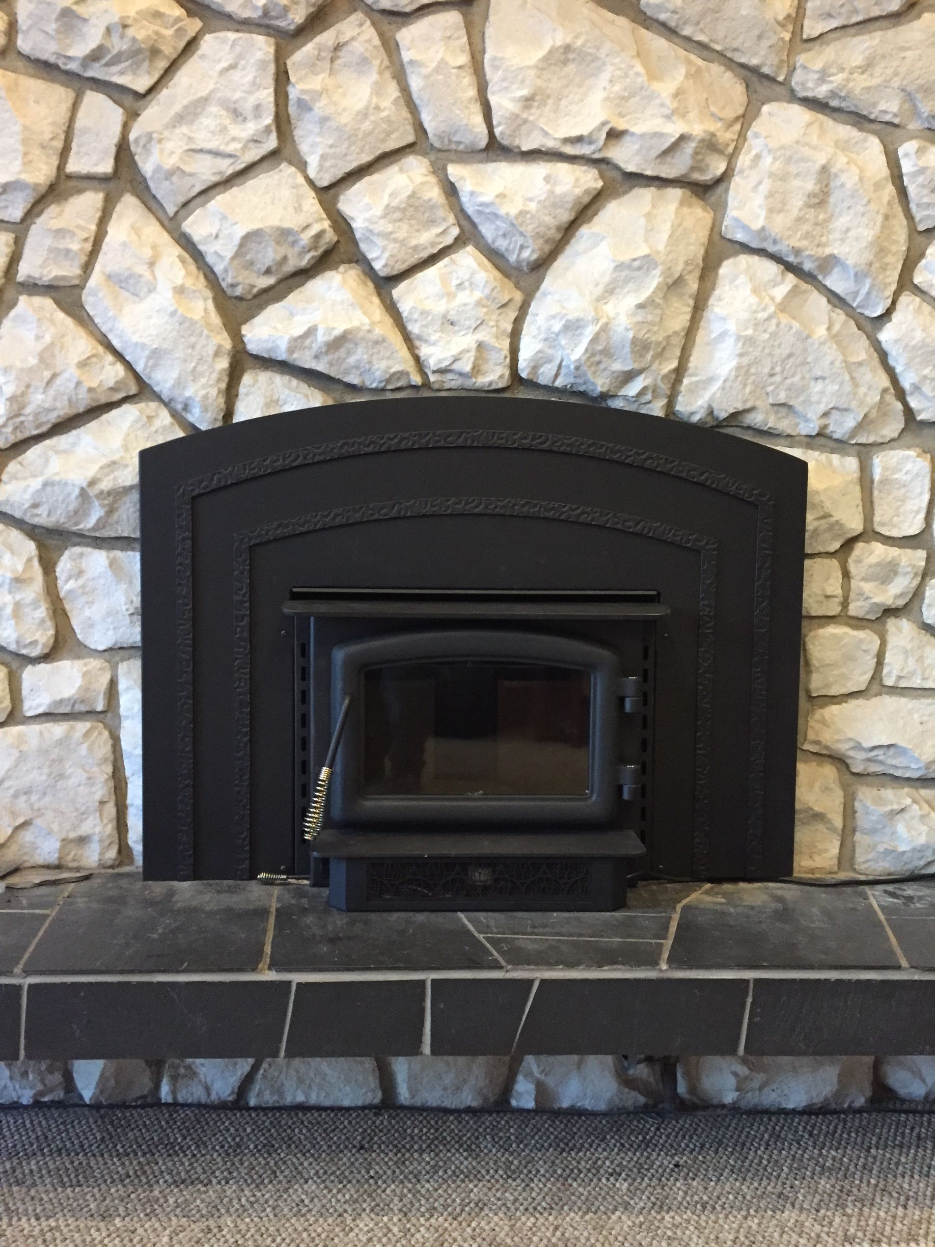 A fireplace with a wood stove in it and a stone wall.