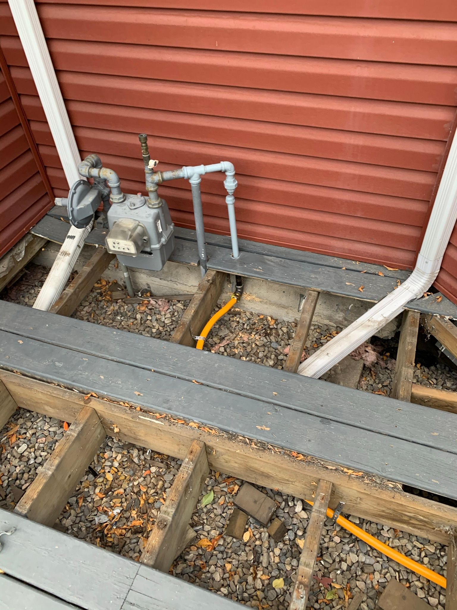 A gas meter is sitting under a wooden deck next to a house.