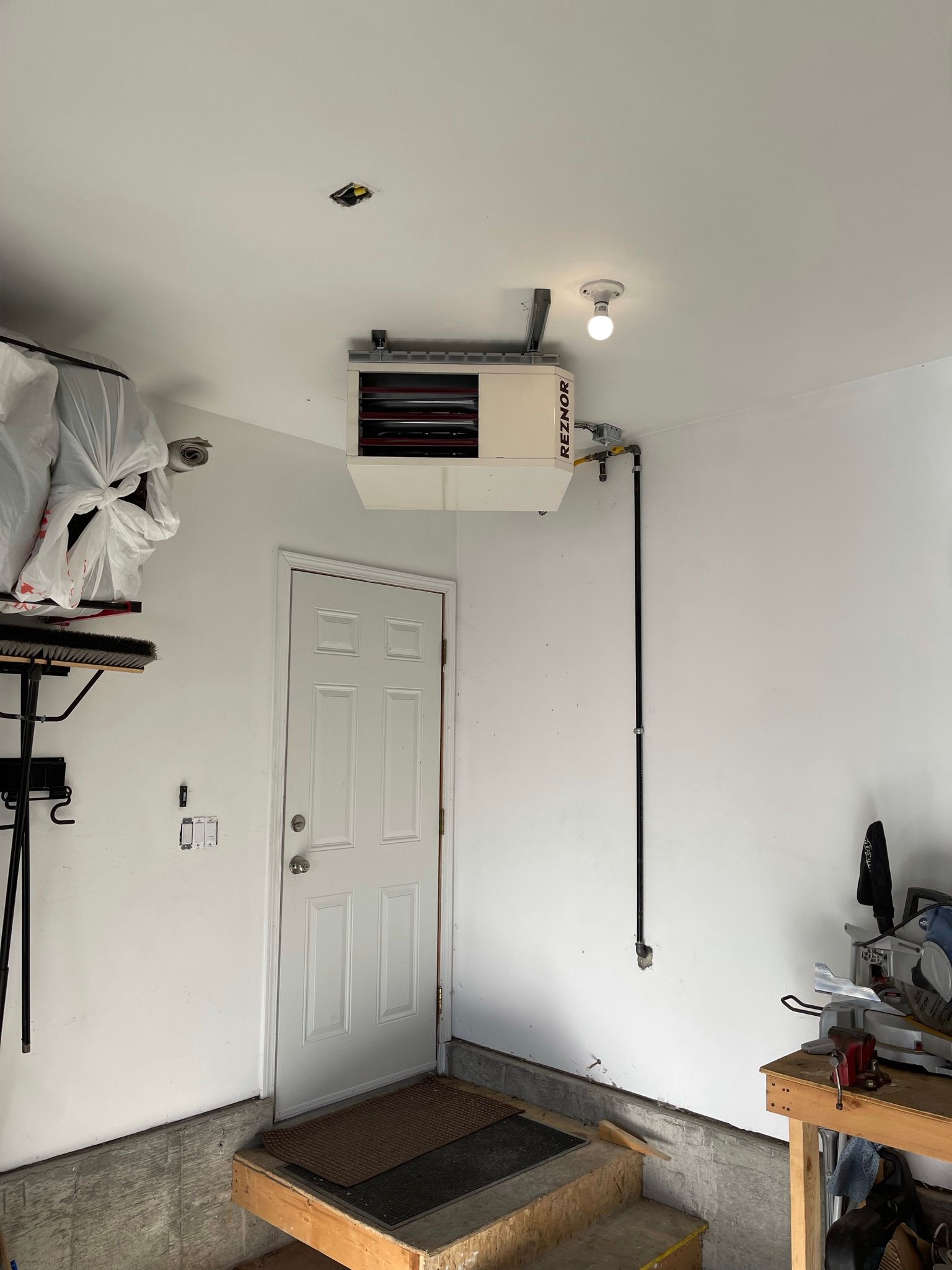 A garage with a door open and a heater hanging from the ceiling.
