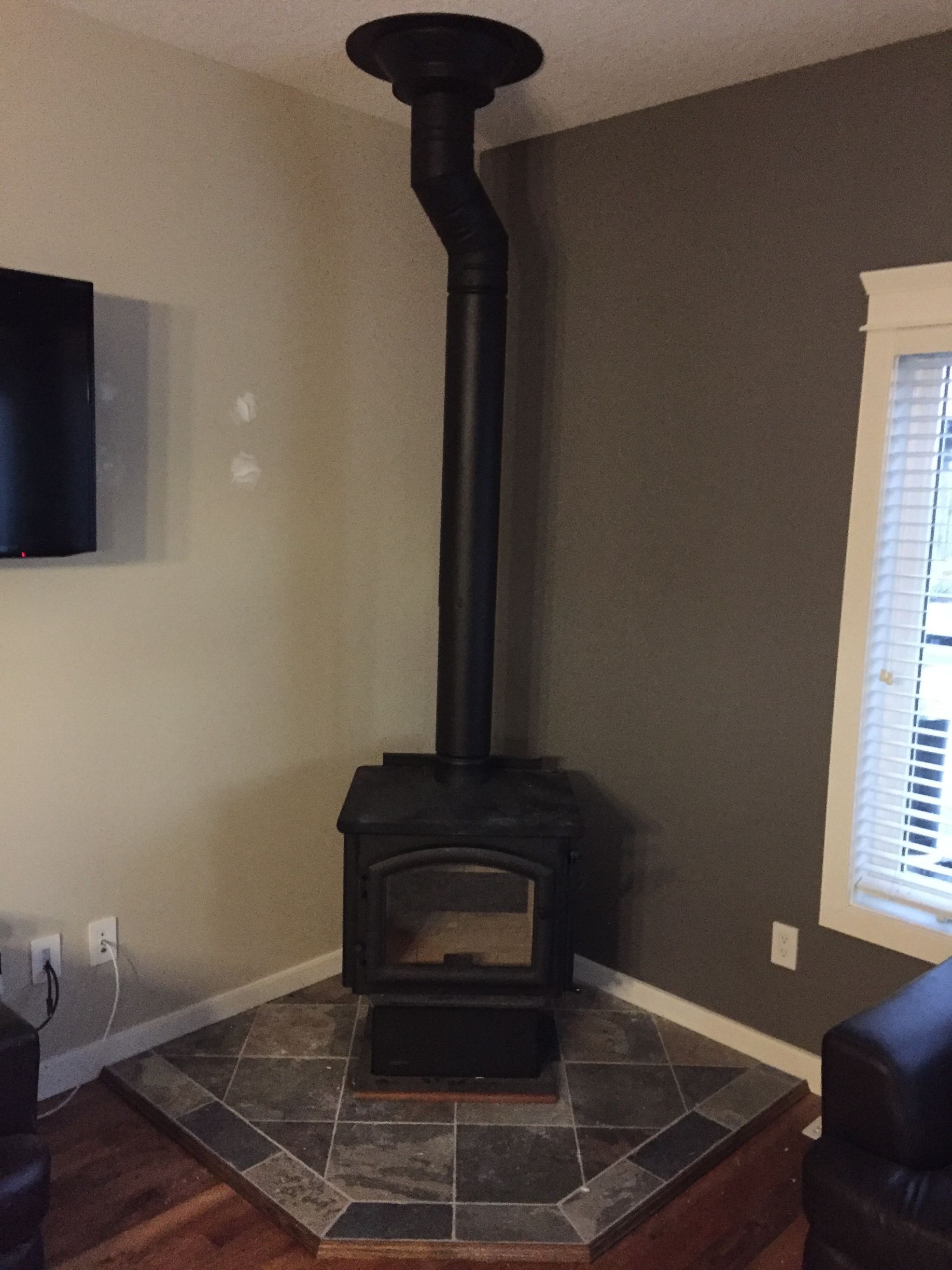 A wood stove is in the corner of a living room next to a window.