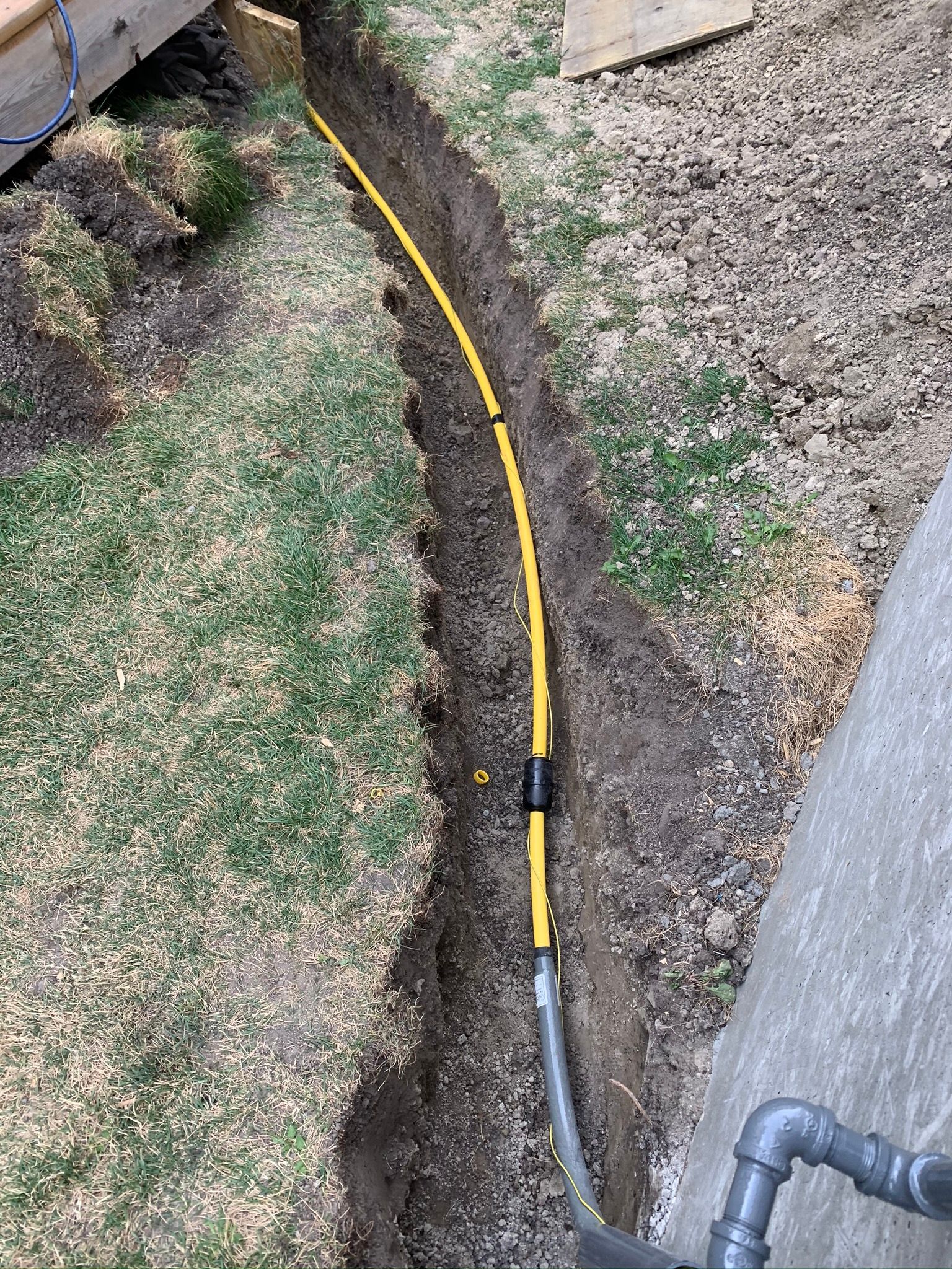A yellow hose is laying in the dirt next to a pipe.