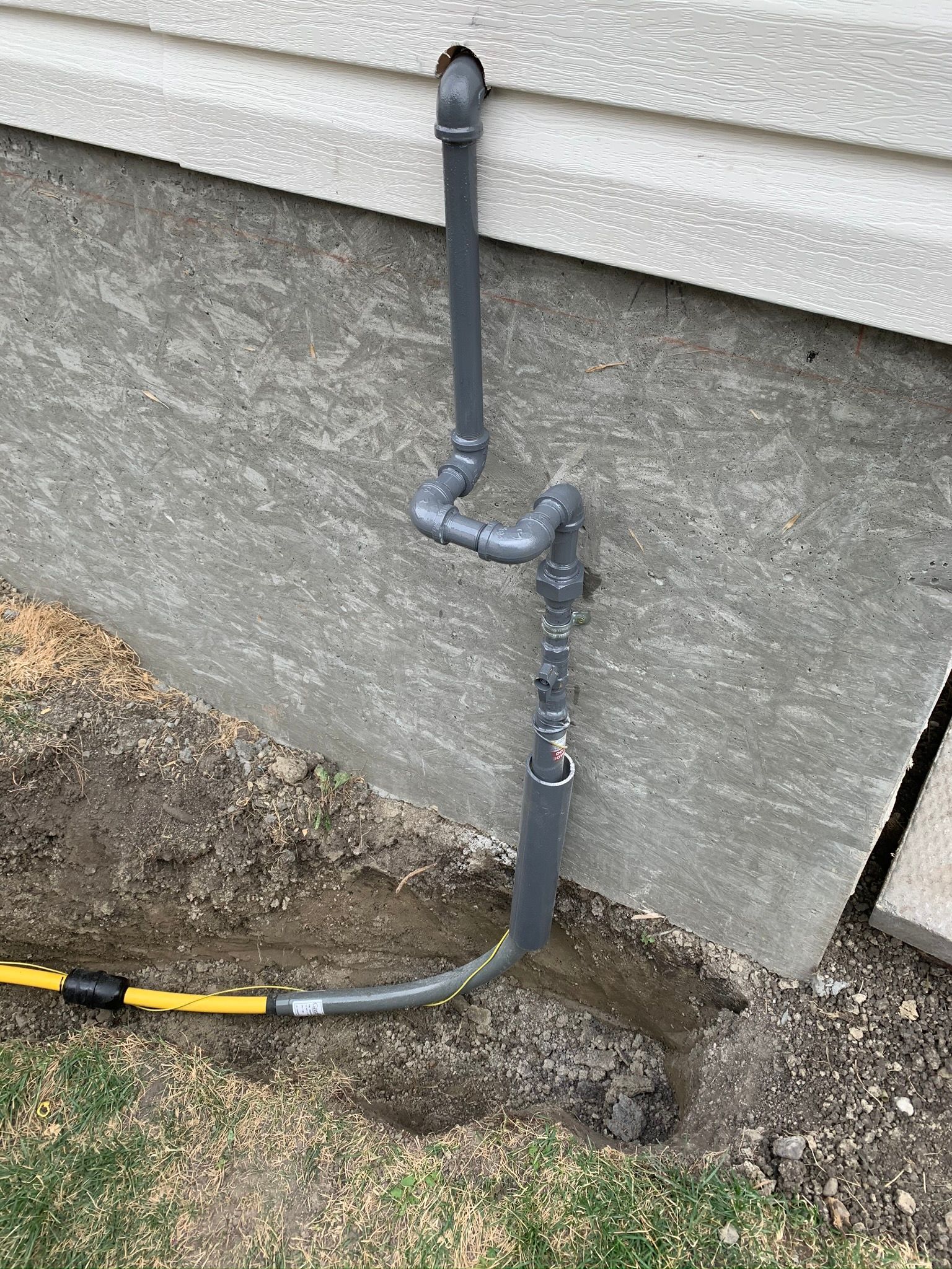 A hose is connected to a pipe on the side of a house.