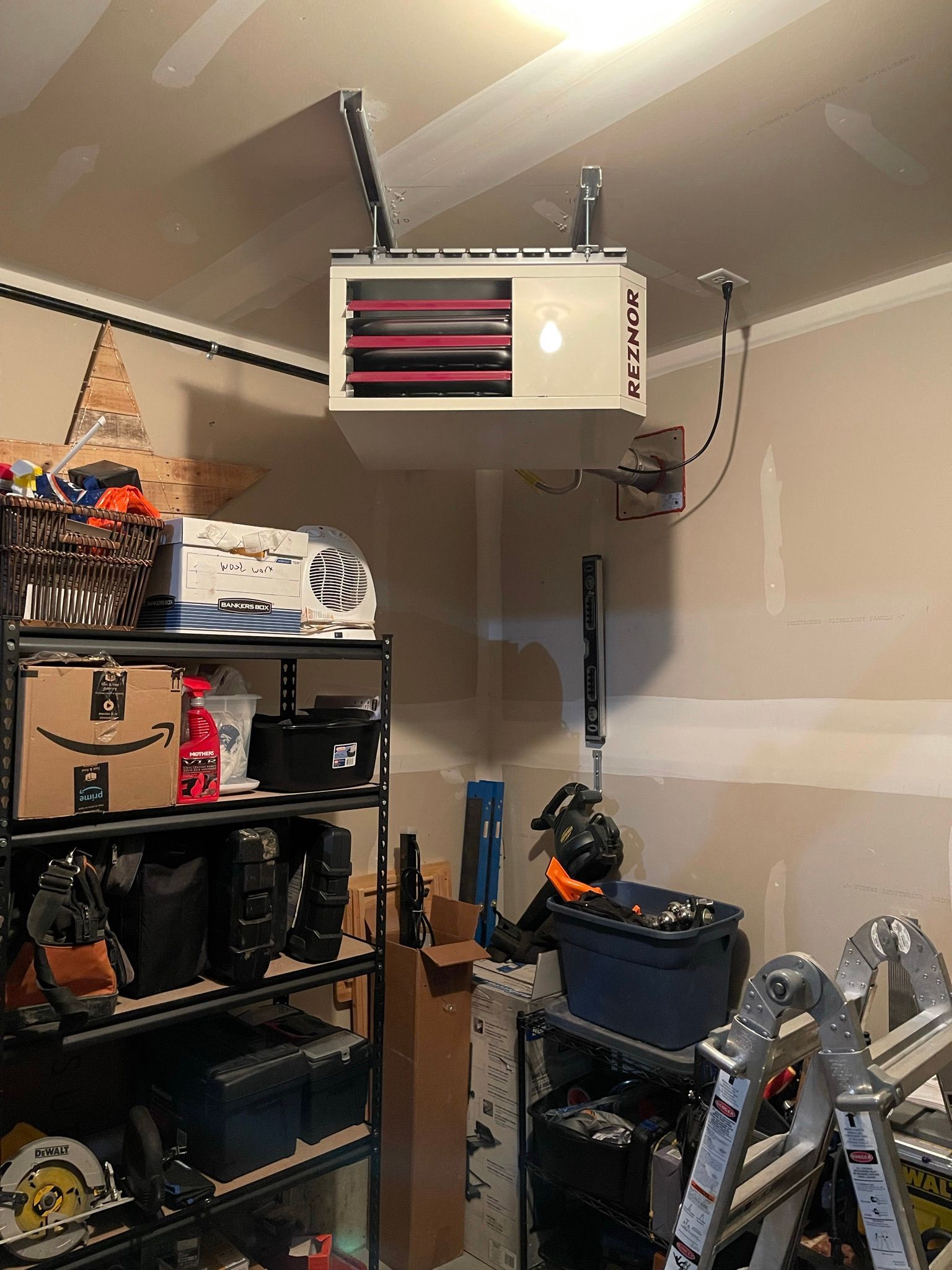 A garage with a heater hanging from the ceiling and a ladder.