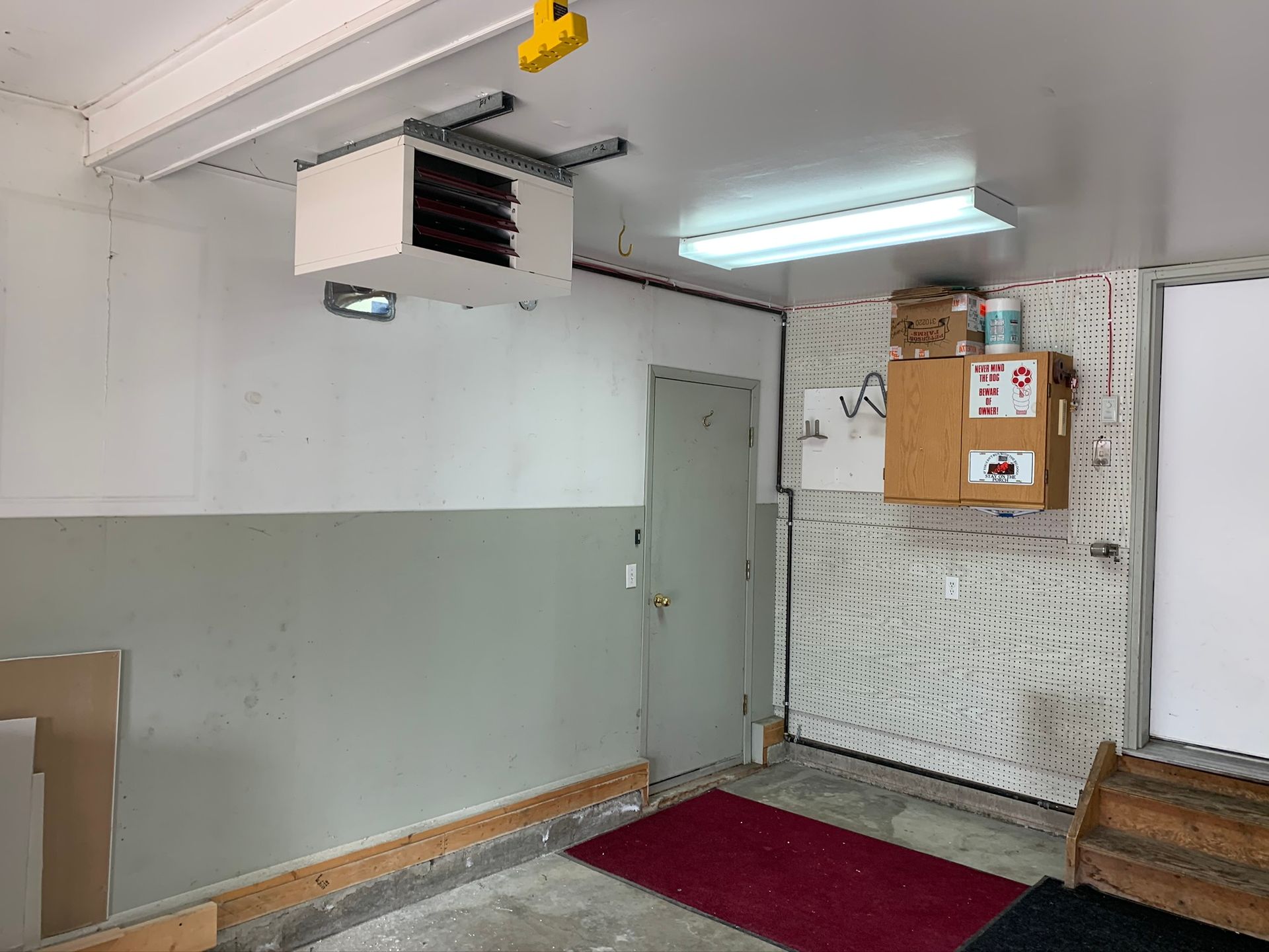 A garage with a heater hanging from the ceiling and a door.