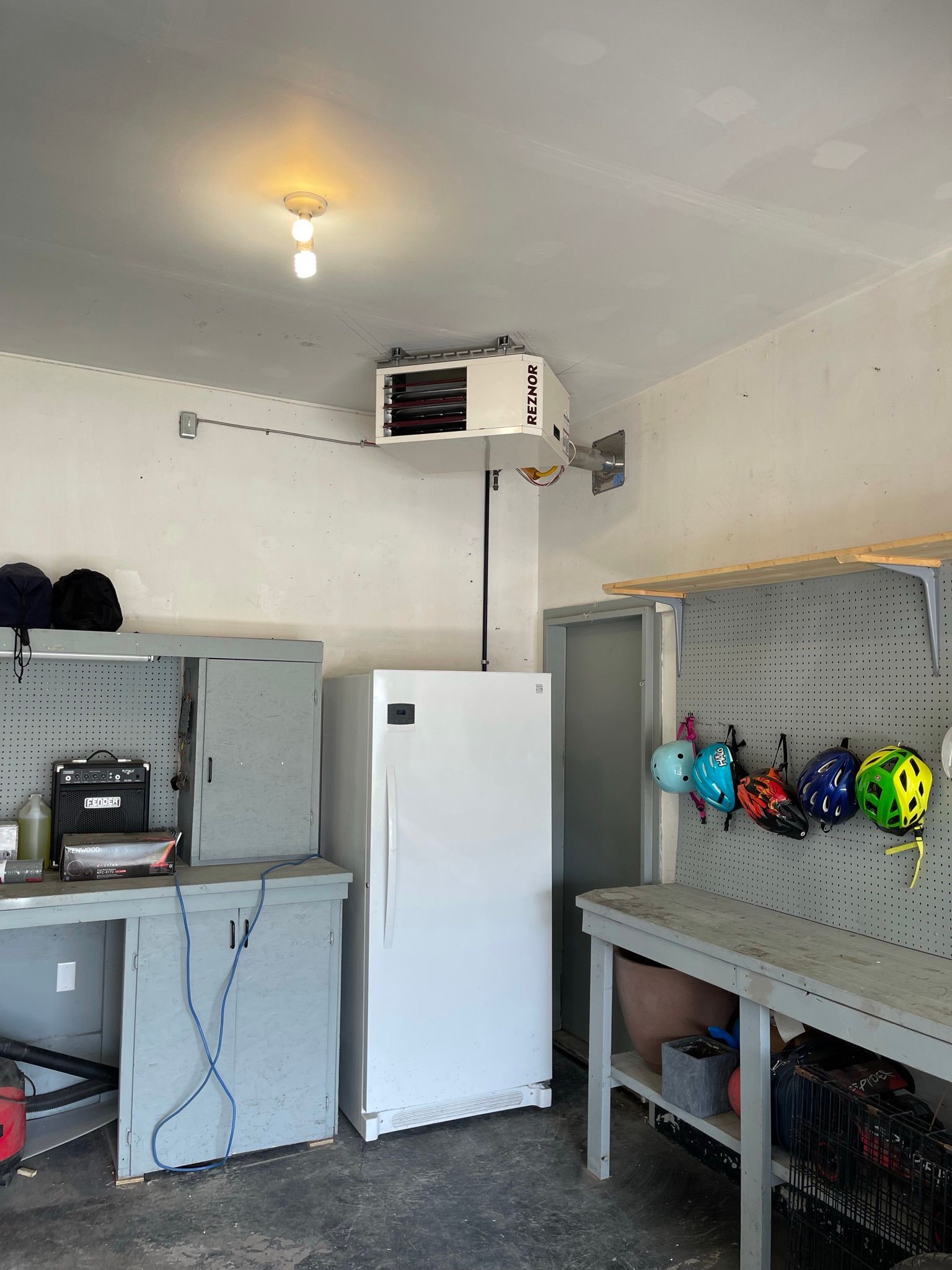 A garage with a refrigerator and a table with helmets hanging on the wall.
