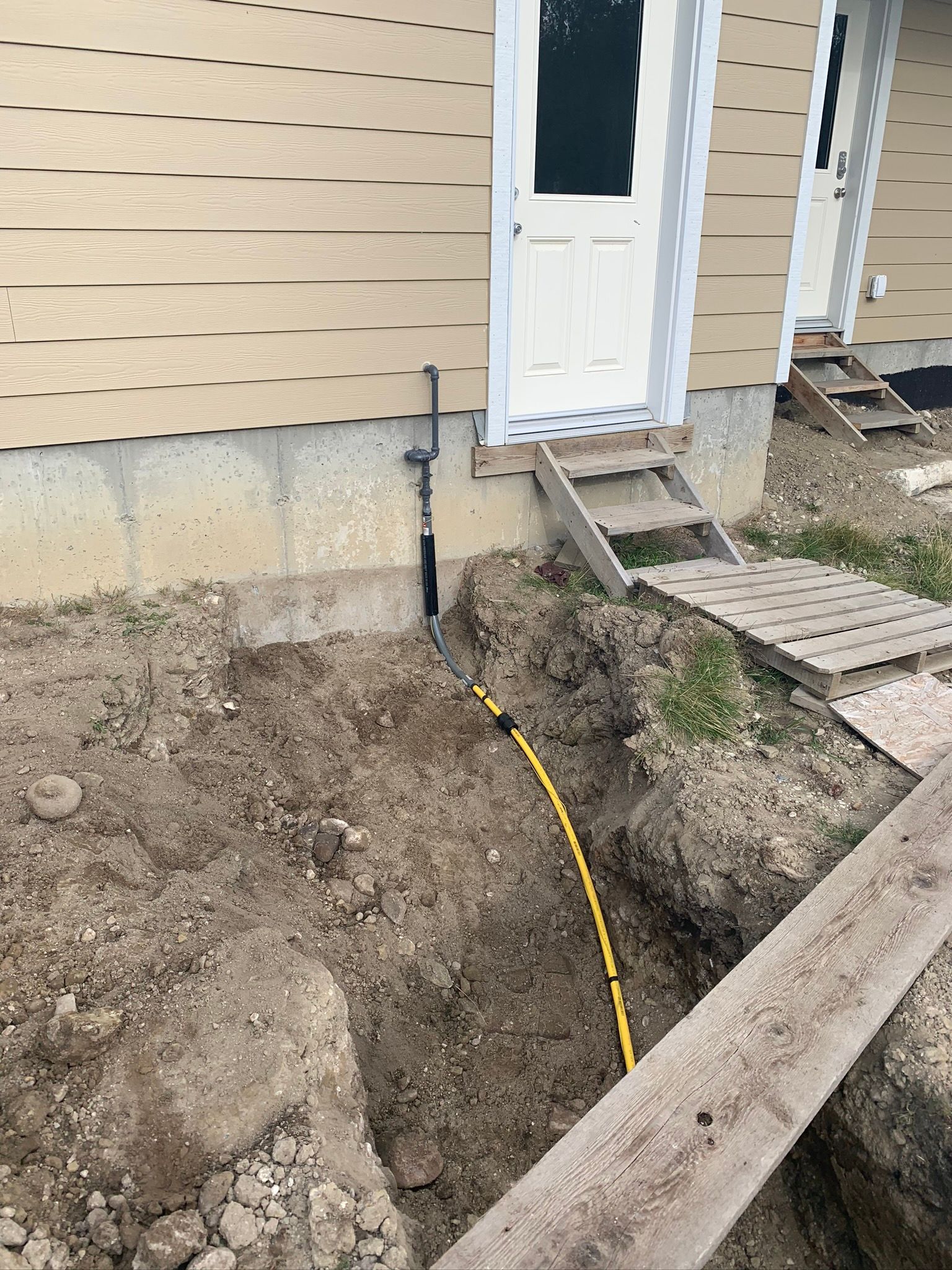 A yellow hose is laying in the dirt in front of a house.