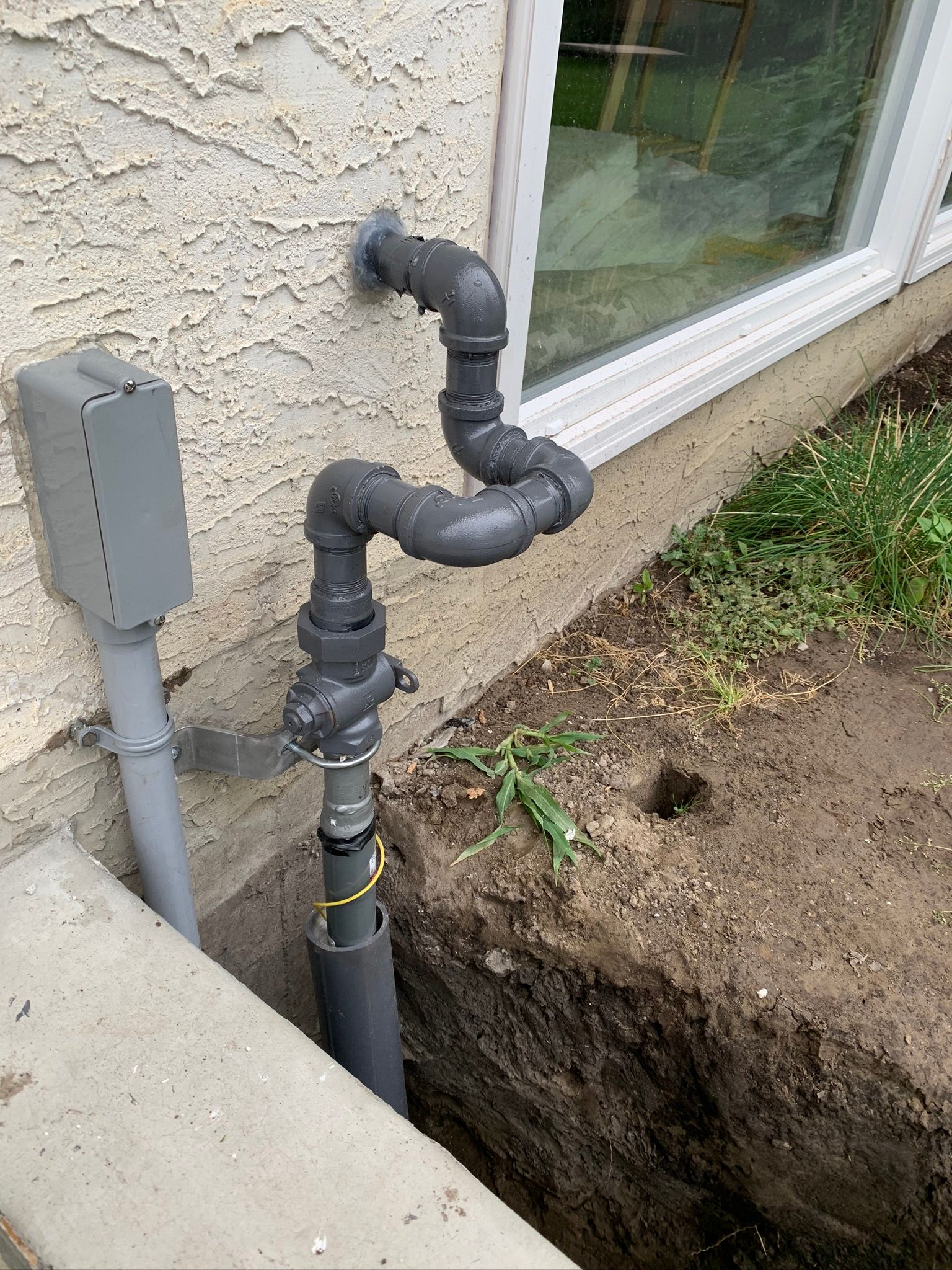 A pipe is being installed on the side of a house next to a window.