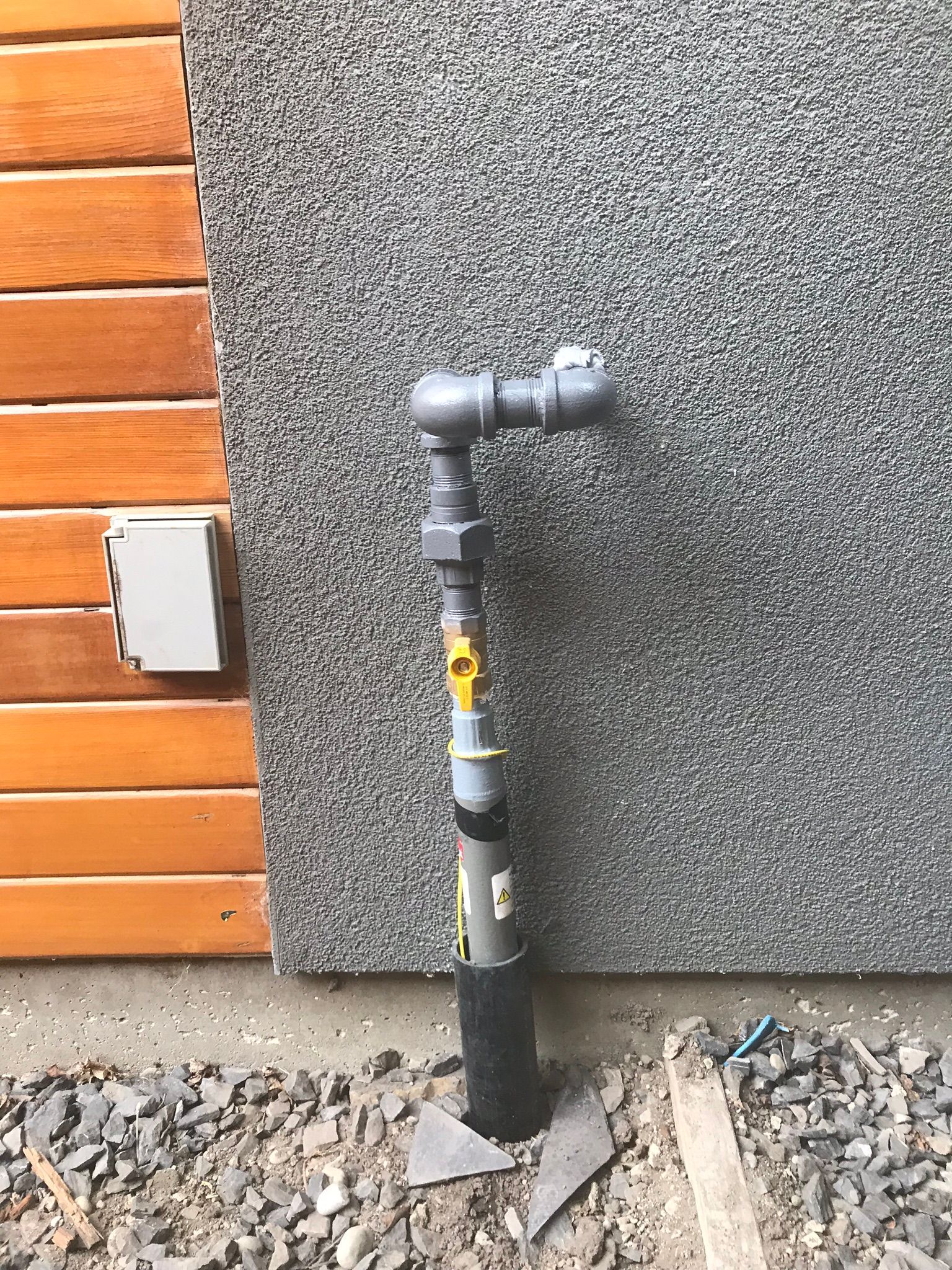 A gray pipe is sitting in front of a wooden wall.