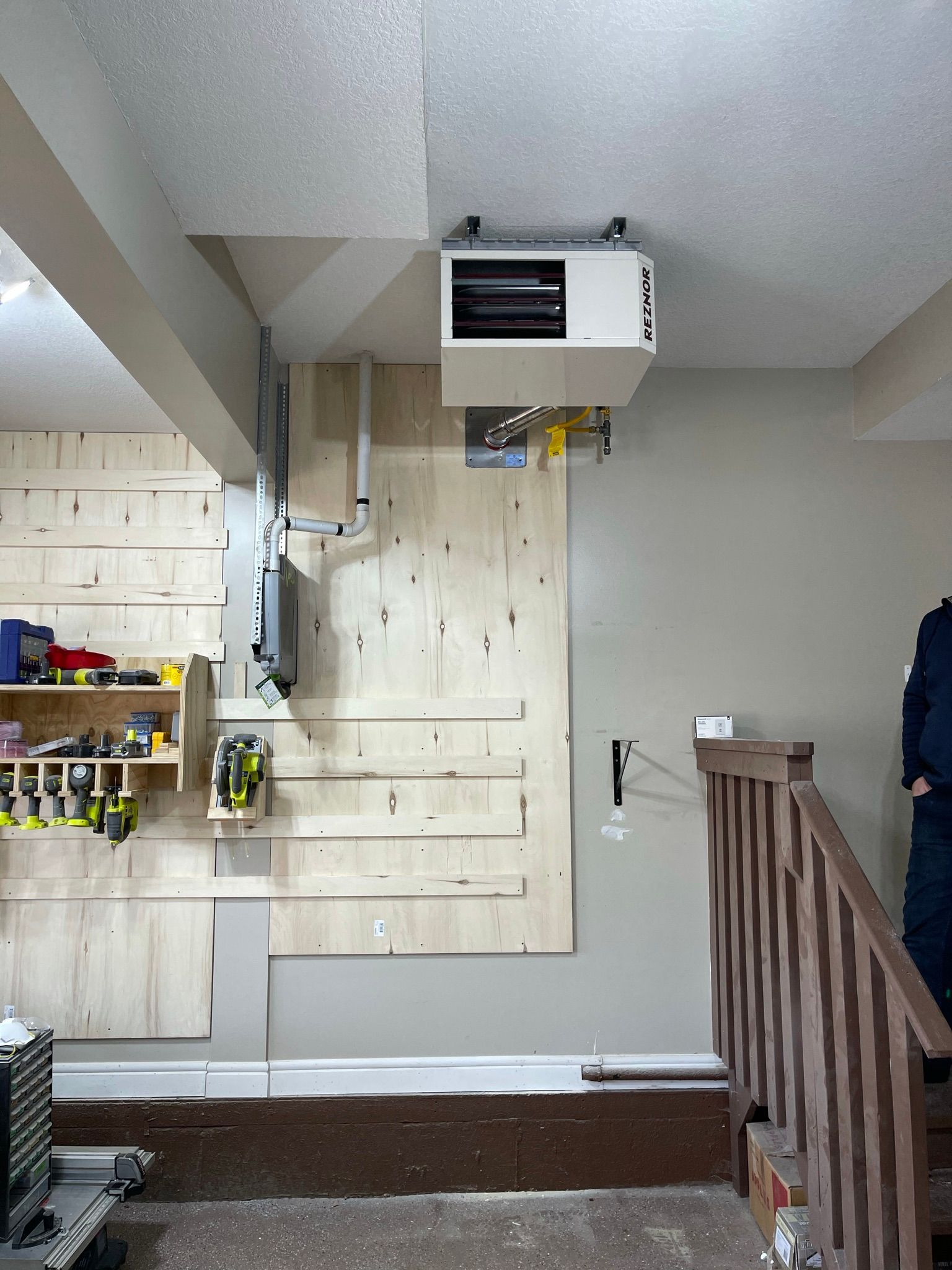 A man is standing in a room with a heater hanging from the ceiling.