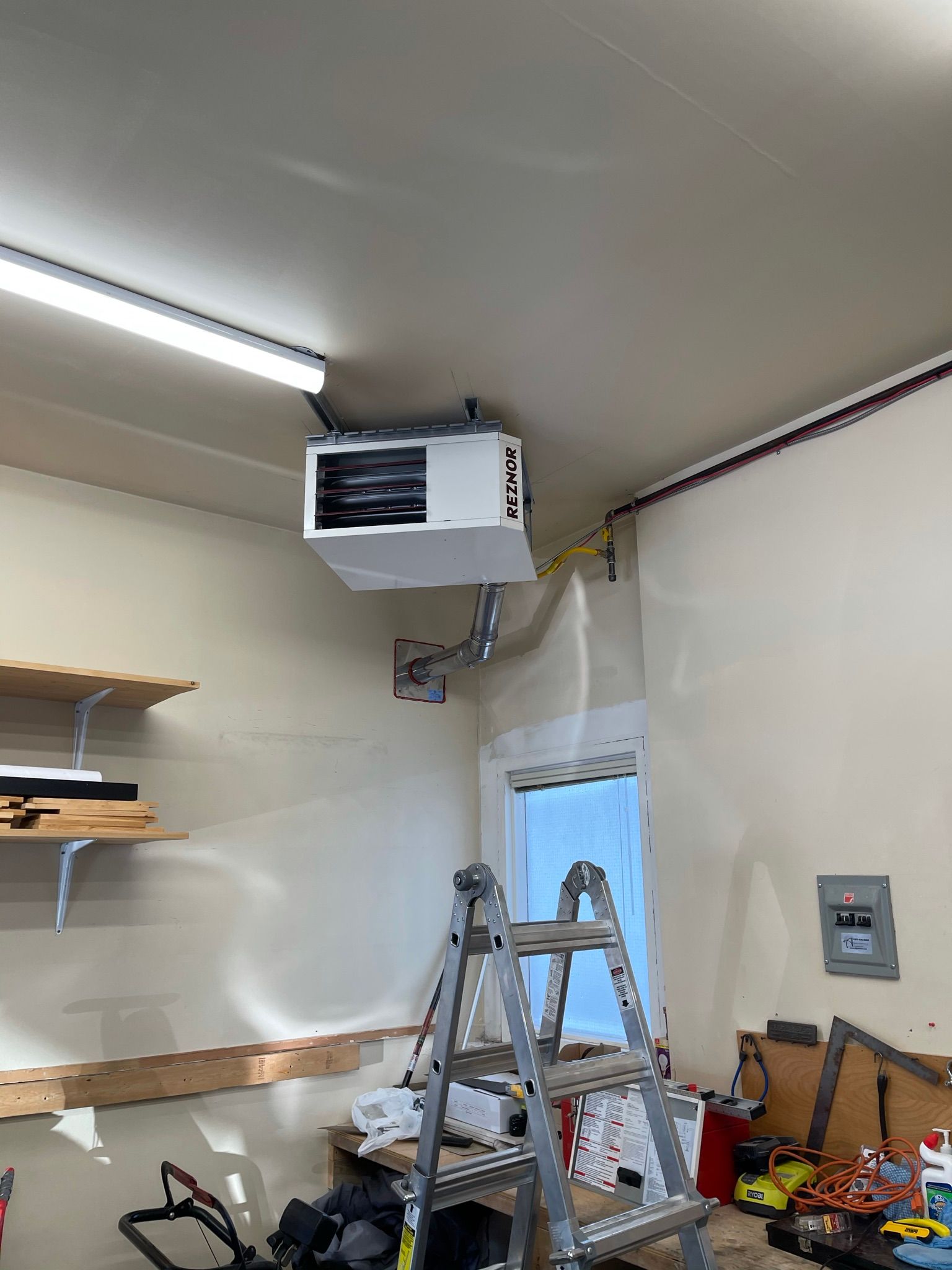 A garage with a ladder and a heater hanging from the ceiling.