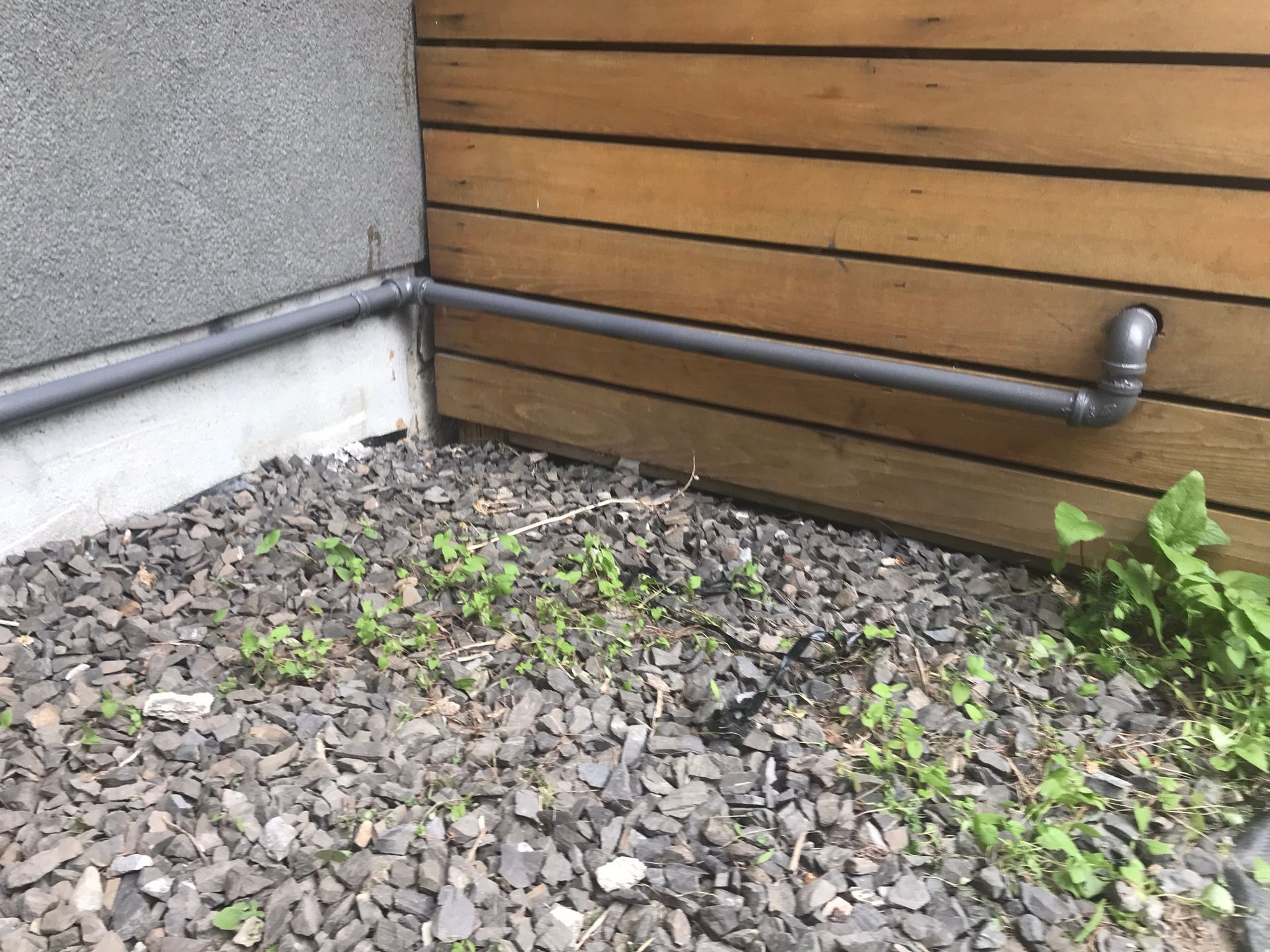 A pipe is connected to a wall next to a pile of gravel.