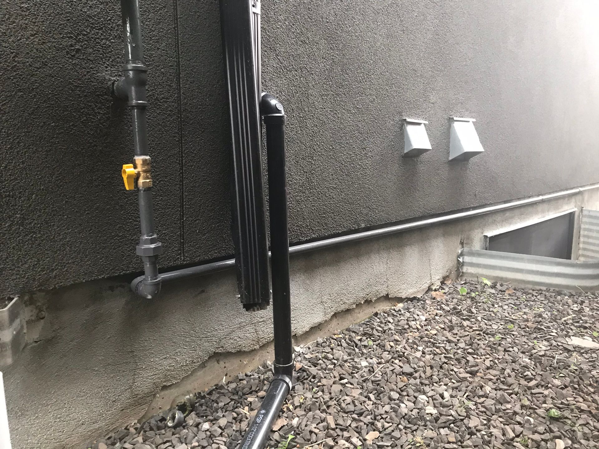 A black pipe is attached to the side of a building.