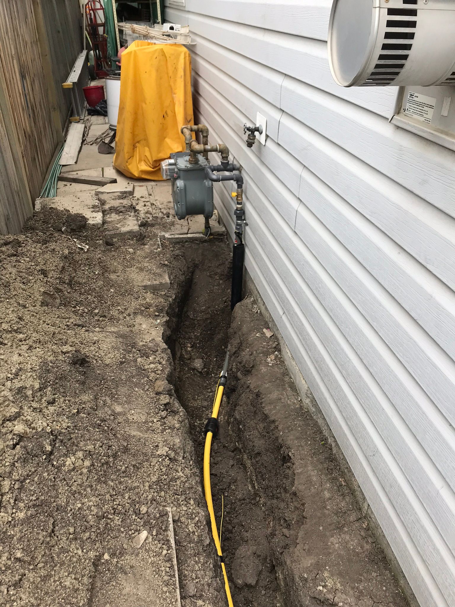 A yellow hose is connected to a gas meter on the side of a house.