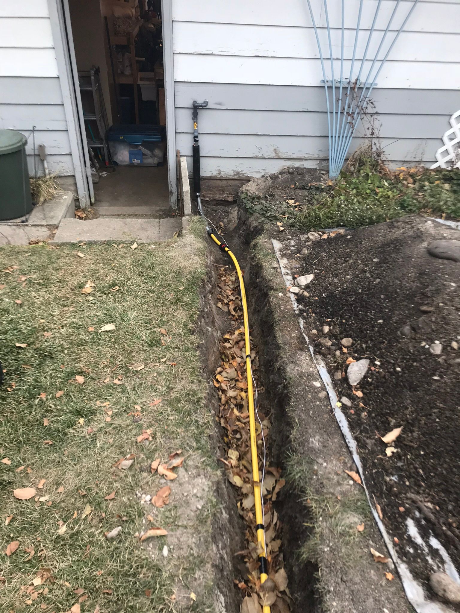 A yellow hose is laying in the dirt next to a house.