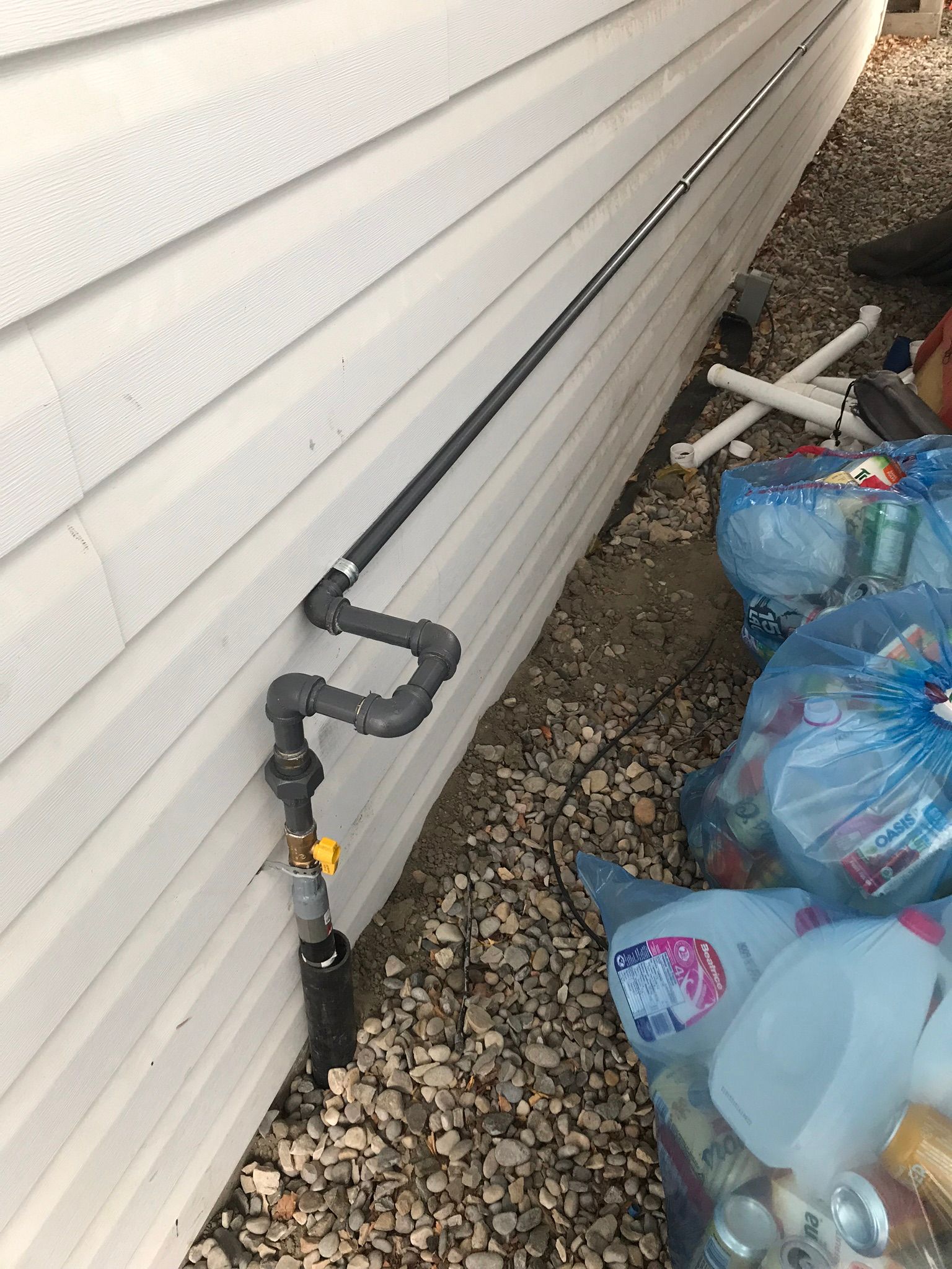 A pipe is attached to the side of a house next to a pile of trash bags.