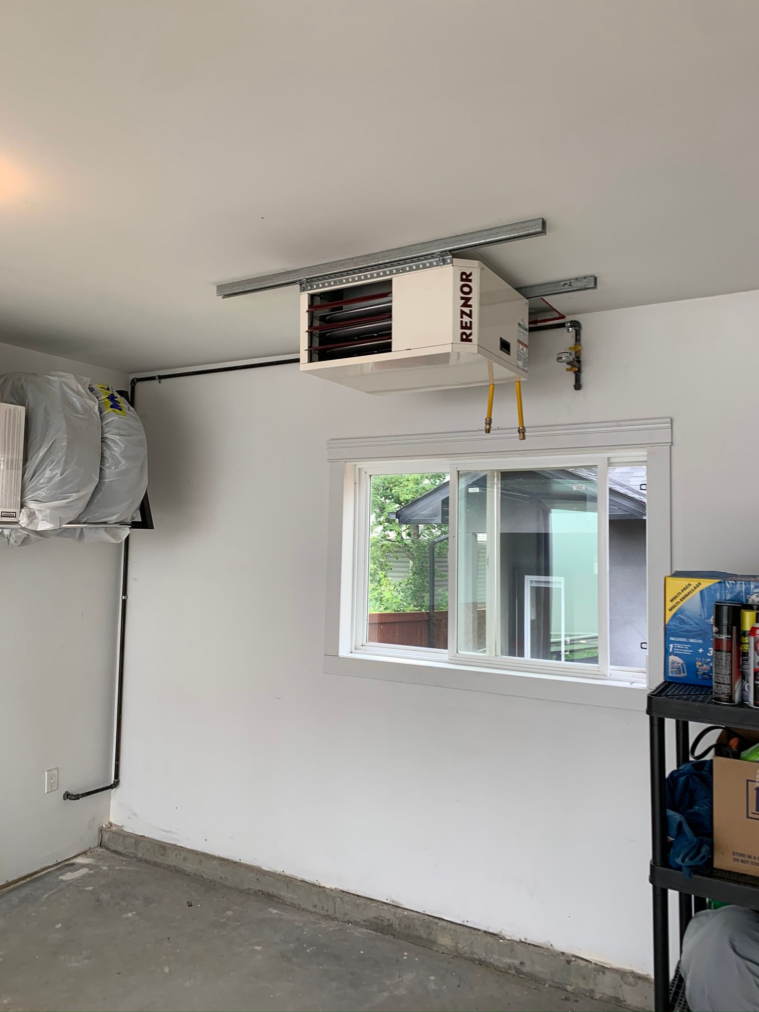 A garage with a heater hanging from the ceiling and a window.