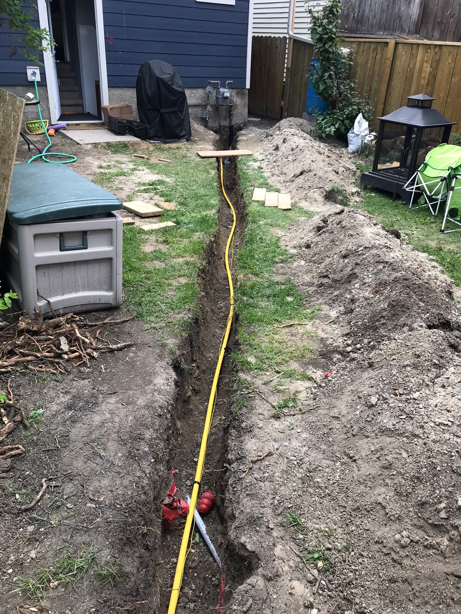 A hose is laying in the dirt in a backyard next to a house.